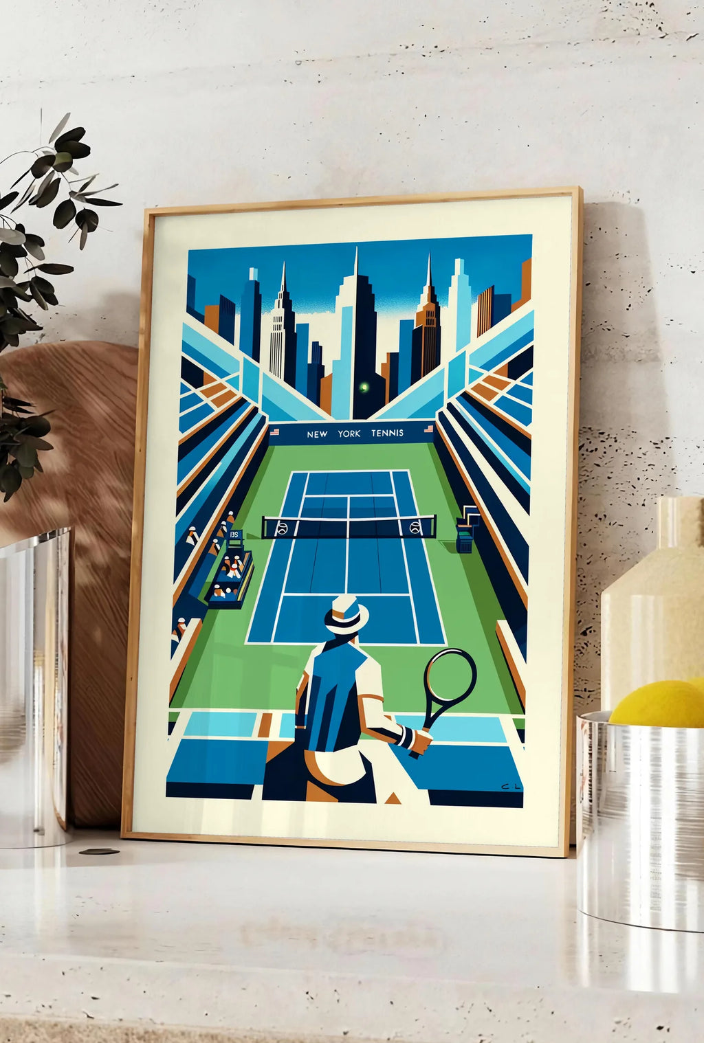 Affiche court de tennis bleu et joueur de dos, posee sur un plan de travail de cuisine en pierre claire, entre une branche d'eucalyptus en vase et un bocal de citrons