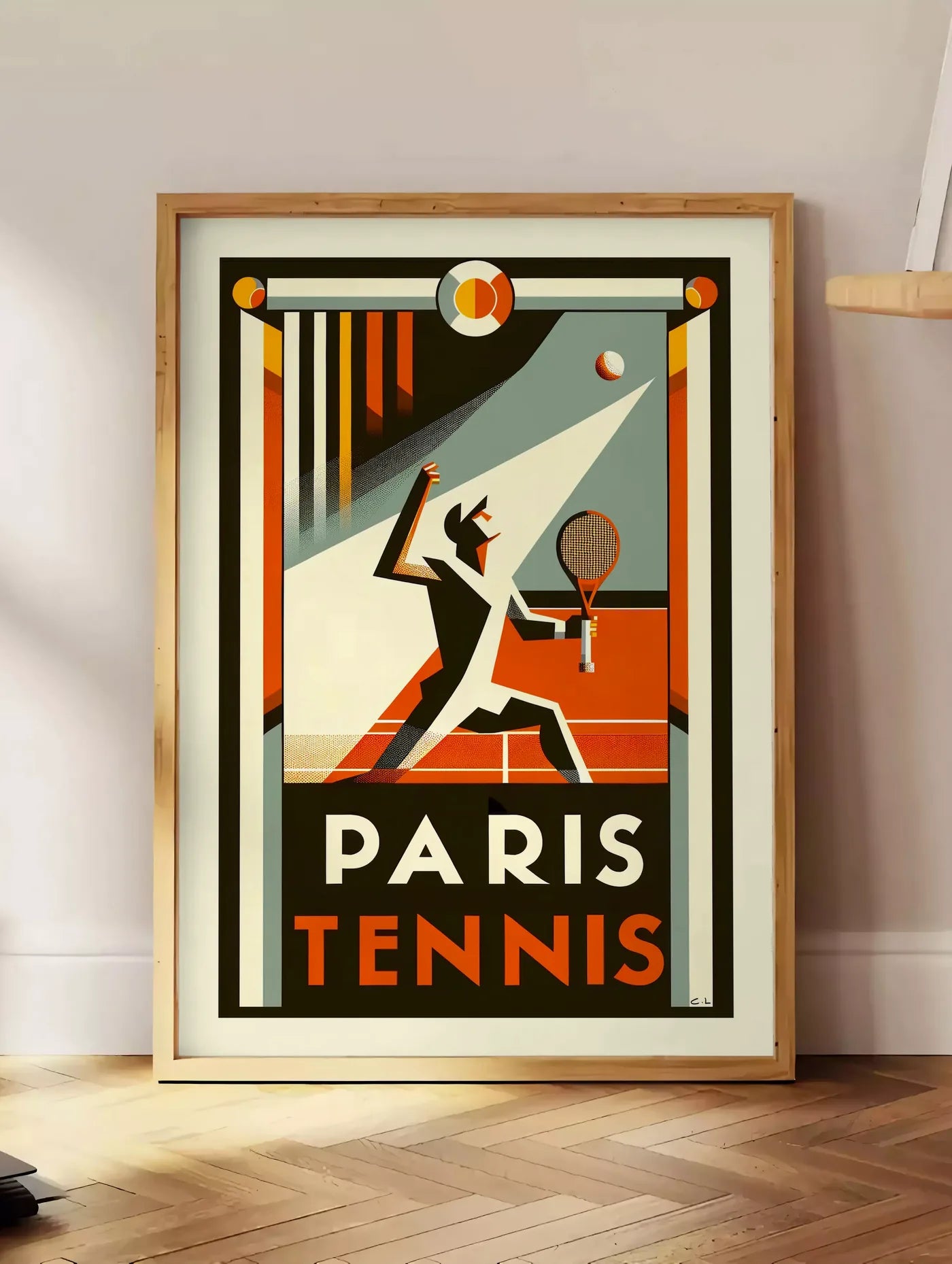 Estampe affiche tennis Paris Art Deco, posee au sol dans un coin salon, sur un parquet a chevrons, pres d'une table d'appoint en chene chargee de livres