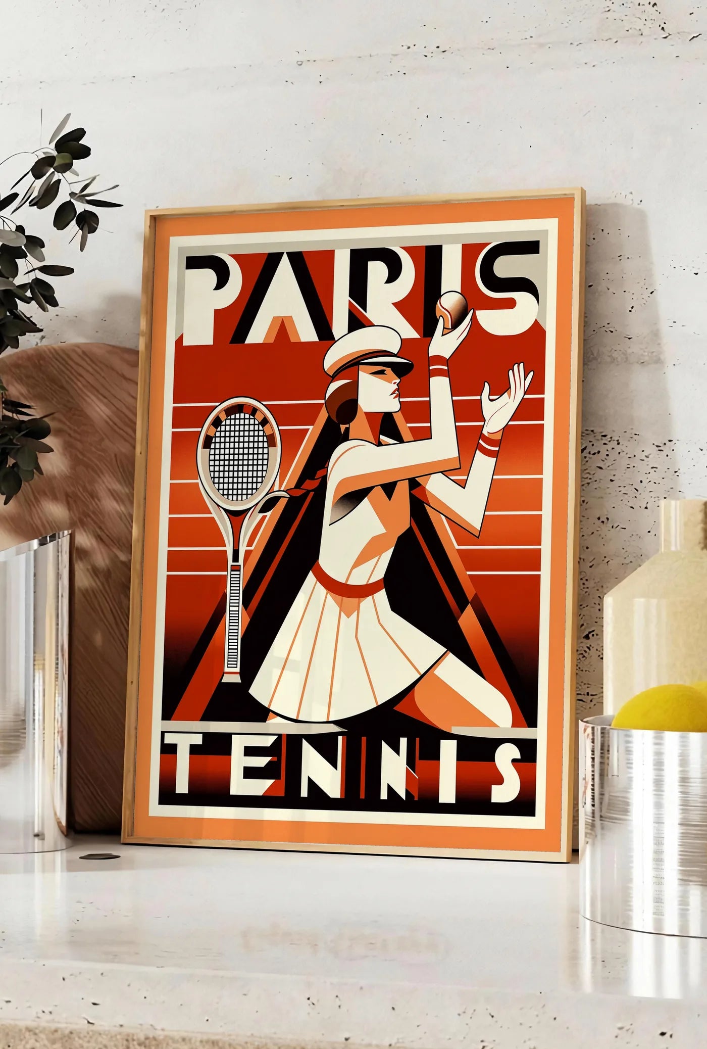 Affiche joueuse de tennis au service avec raquette, posee sur un plan de travail de cuisine en pierre claire, entre une branche d'eucalyptus en vase et un bocal de citrons