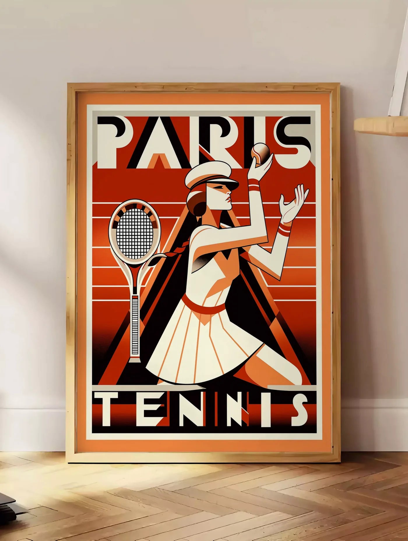 Estampe joueuse de tennis au service avec raquette, posee au sol dans un coin salon, sur un parquet a chevrons, pres d'une table d'appoint en chene chargee de livres