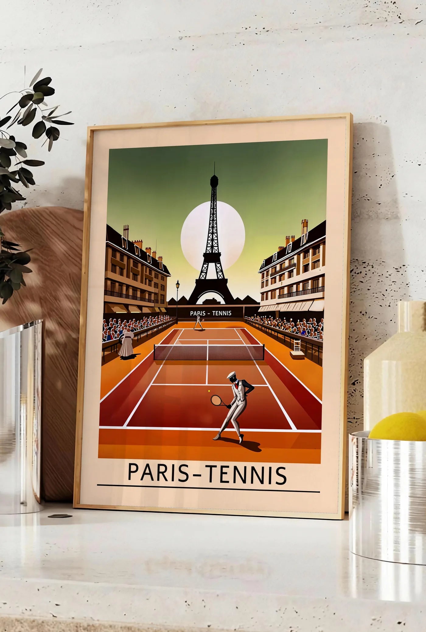 Affiche joueur de tennis sur terre battue, posee sur un plan de travail de cuisine en pierre claire, entre une branche d'eucalyptus en vase et un bocal de citrons