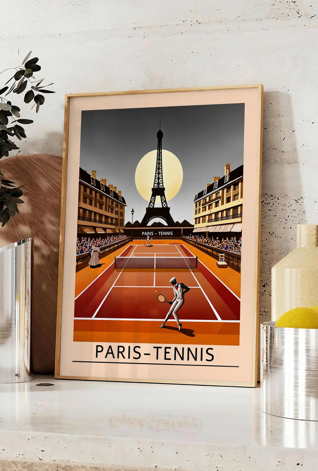 Affiche joueur de tennis sur terre battue, posee sur un plan de travail de cuisine en pierre claire, entre une branche d'eucalyptus en vase et un bocal de citrons