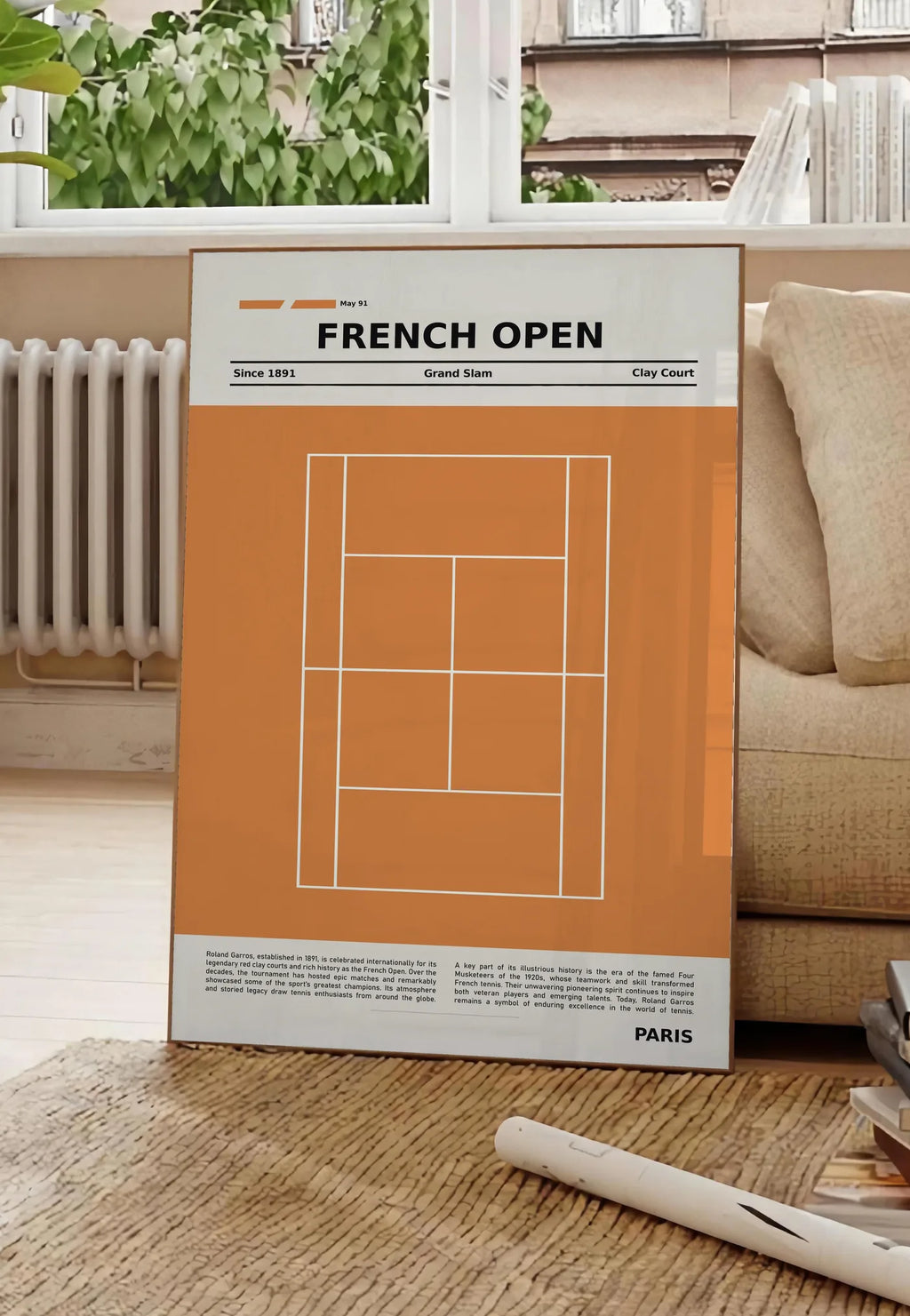 Poster court de tennis stylisé en terre battue avec titre FRENCH OPEN, posee au sol dans un salon parisien, devant une grande fenetre donnant sur un immeuble haussmannien, entre un ficus et un canape creme