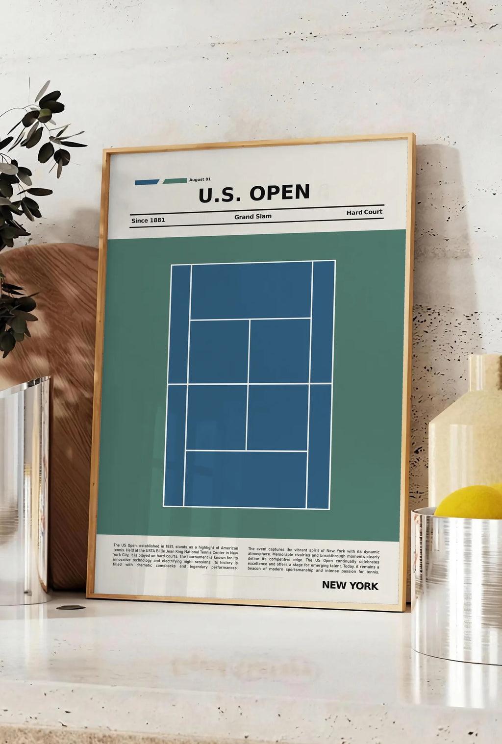Affiche plan de court de tennis en dur bleu, posee sur un plan de travail de cuisine en pierre claire, entre une branche d'eucalyptus en vase et un bocal de citrons