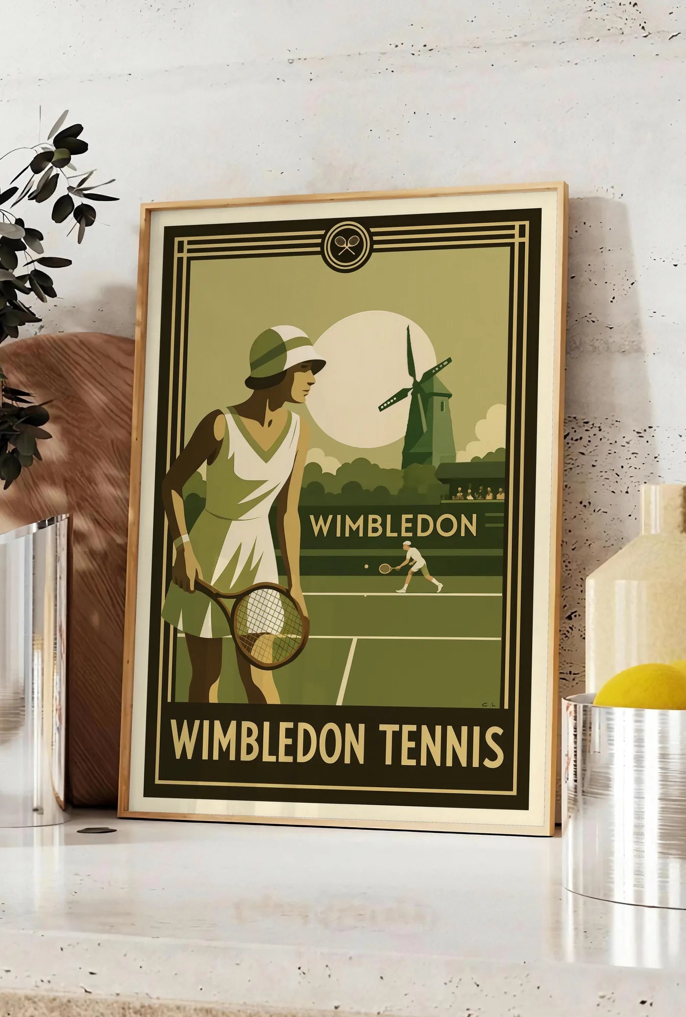 Affiche joueuse de tennis 1920 et raquette en bois, posee sur un plan de travail de cuisine en pierre claire, entre une branche d'eucalyptus en vase et un bocal de citrons