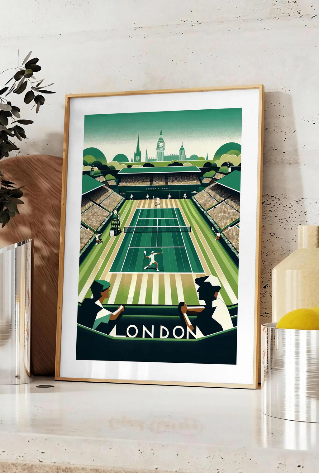 Affiche joueur de tennis sur gazon et spectateurs, posee sur un plan de travail de cuisine en pierre claire, entre une branche d'eucalyptus en vase et un bocal de citrons
