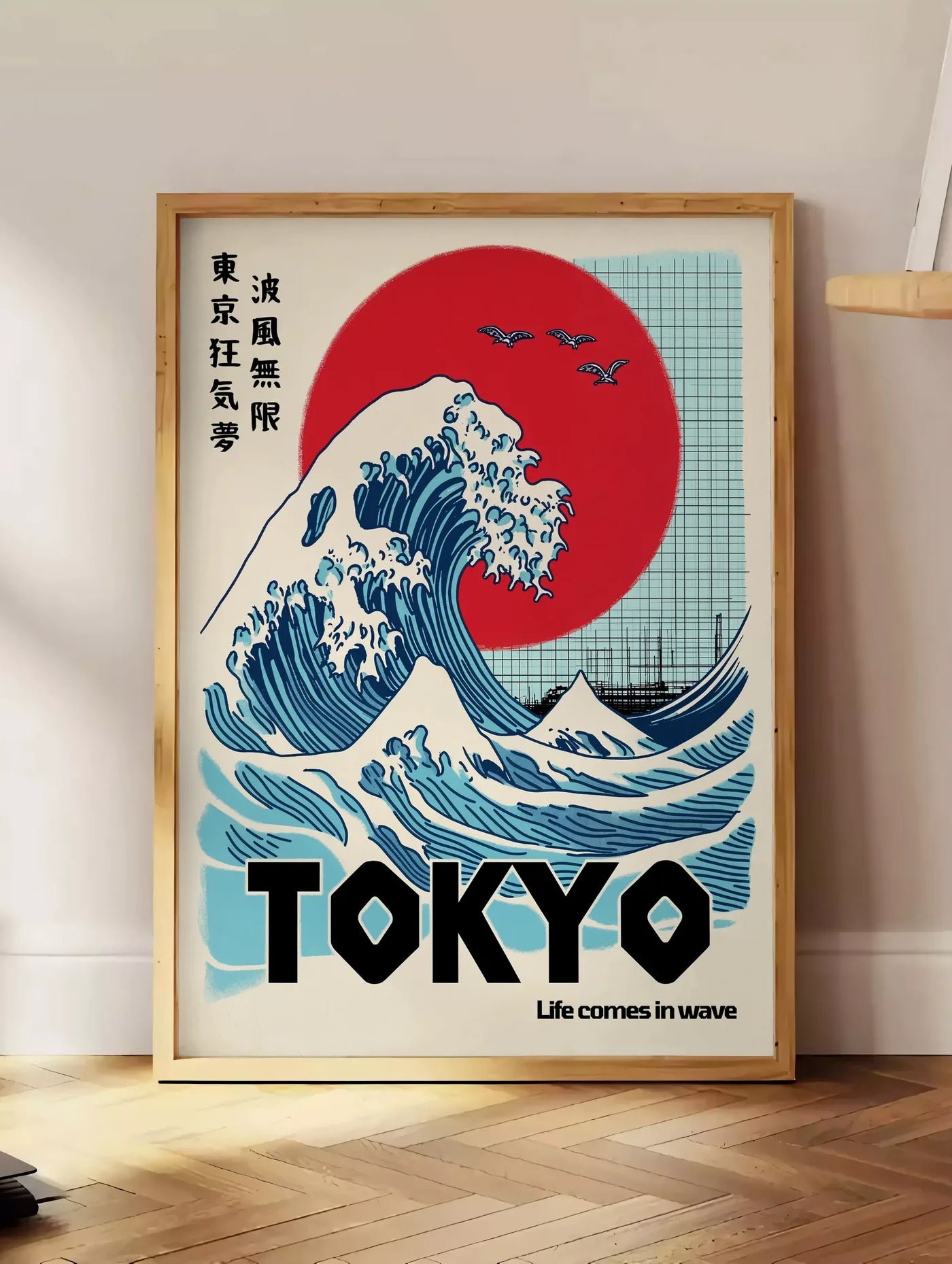 Estampe affiche vague de Tokyo et soleil rouge art japonais, posee au sol dans un coin salon, sur un parquet a chevrons, pres d'une table d'appoint en chene chargee de livres