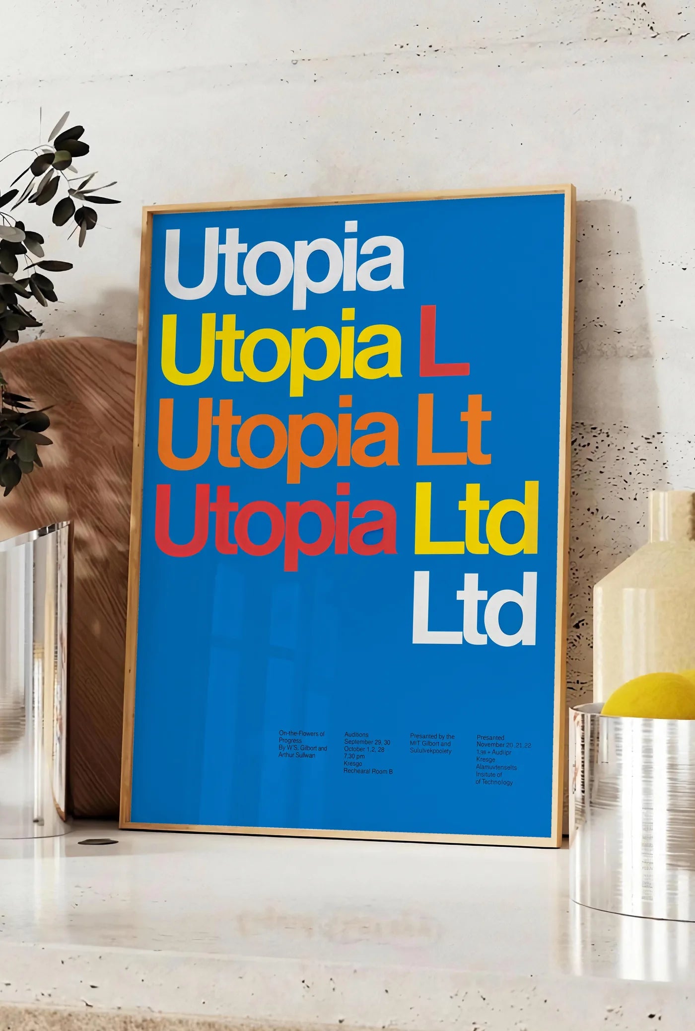 Affiche typographie Utopia Ltd repetee en blanc jaune et rouge sur bleu, posee sur un plan de travail de cuisine en pierre claire, entre une branche d'eucalyptus en vase et un bocal de citrons