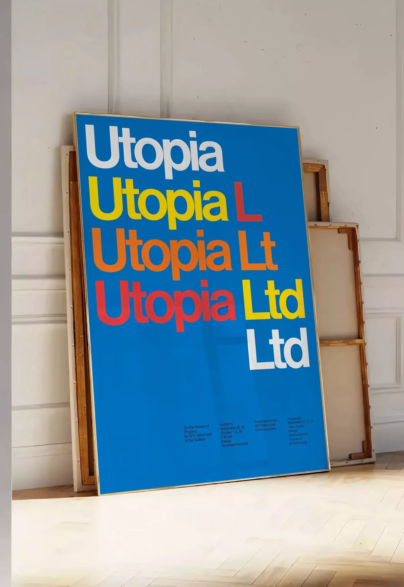 Tirage encadrable typographie Utopia Ltd repetee en blanc jaune et rouge sur bleu, posee au sol dans une entree lumineuse, contre un mur a panneaux blancs, a cote de chassis en bois empiles
