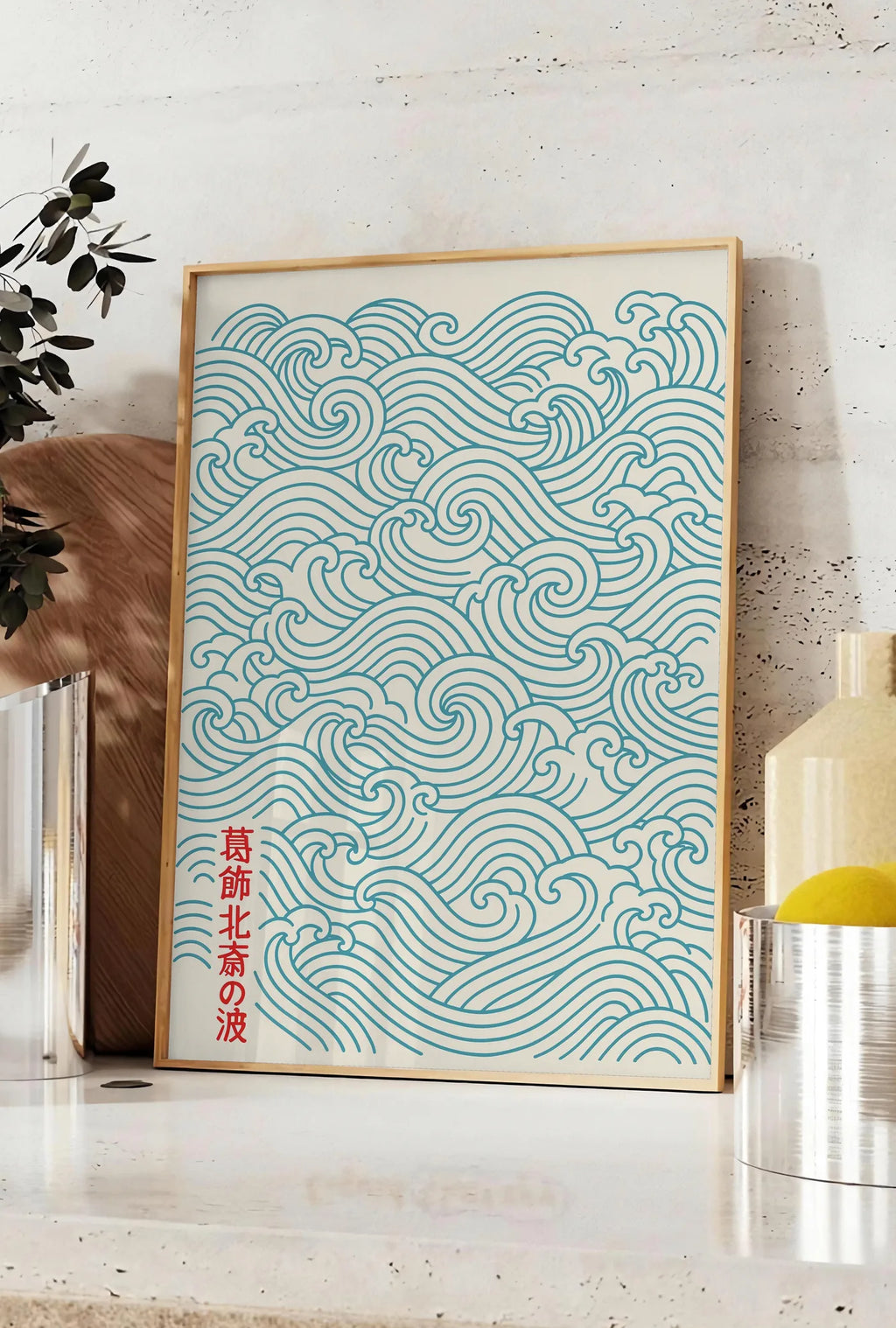 Affiche affiche vagues japonaises motif seigaiha au trait bleu sarcelle sur creme, posee sur un plan de travail de cuisine en pierre claire, entre une branche d'eucalyptus en vase et un bocal de citrons