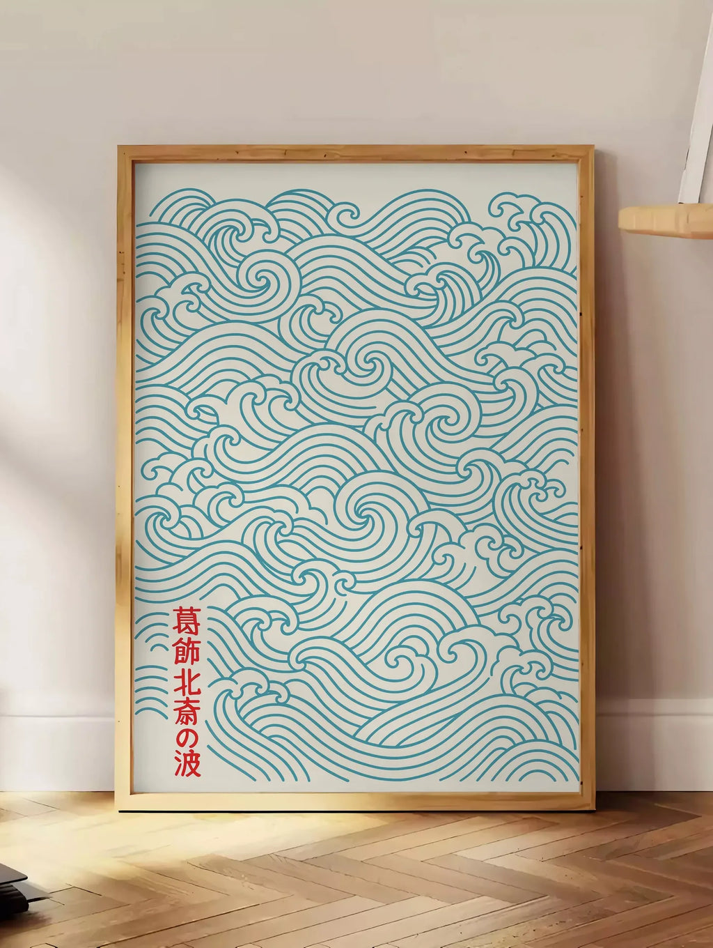 Estampe affiche vagues japonaises motif seigaiha au trait bleu sarcelle sur creme, posee au sol dans un coin salon, sur un parquet a chevrons, pres d'une table d'appoint en chene chargee de livres