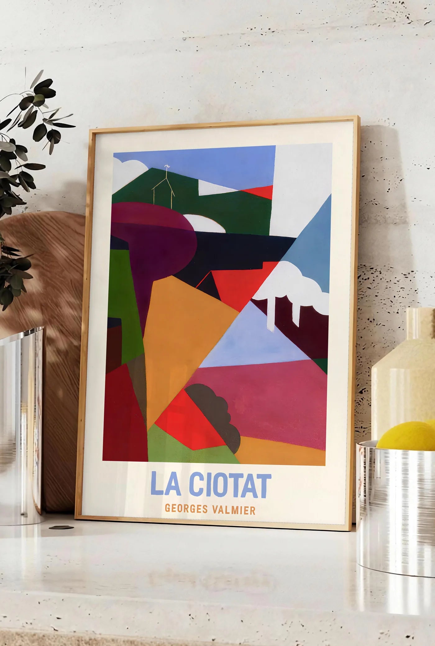 Affiche affiche La Ciotat cubiste, posee sur un plan de travail de cuisine en pierre claire, entre une branche d'eucalyptus en vase et un bocal de citrons