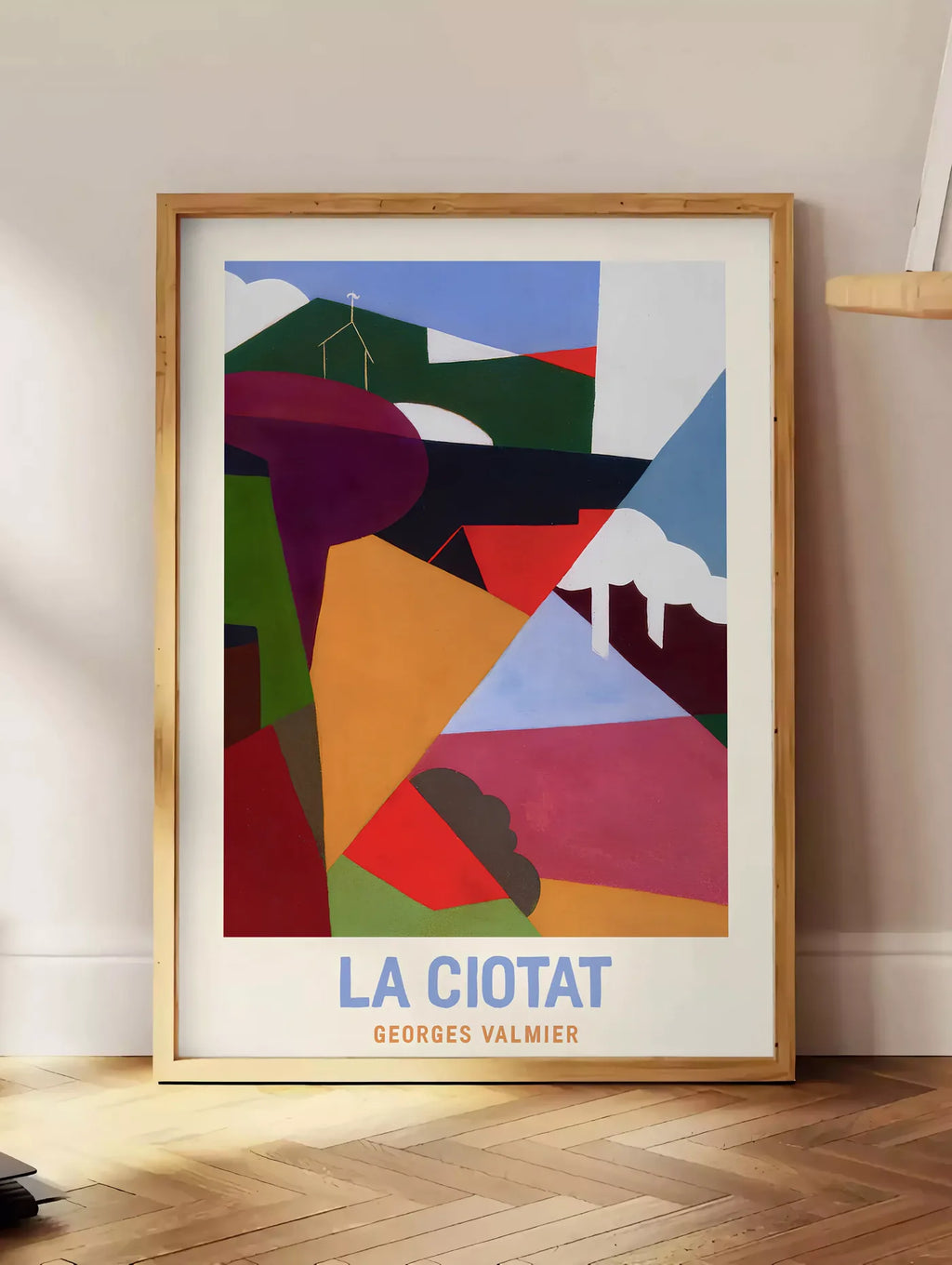 Estampe affiche La Ciotat cubiste, posee au sol dans un coin salon, sur un parquet a chevrons, pres d'une table d'appoint en chene chargee de livres