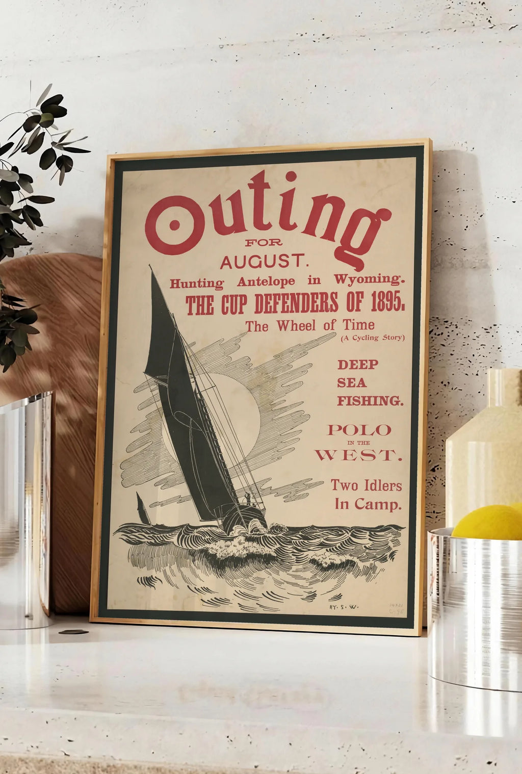 Affiche affiche Outing vintage, posee sur un plan de travail de cuisine en pierre claire, entre une branche d'eucalyptus en vase et un bocal de citrons