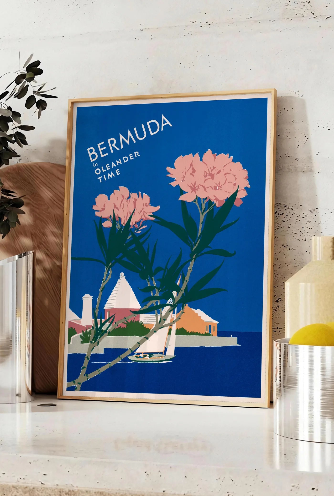 Affiche affiche Bermudes vintage, posee sur un plan de travail de cuisine en pierre claire, entre une branche d'eucalyptus en vase et un bocal de citrons