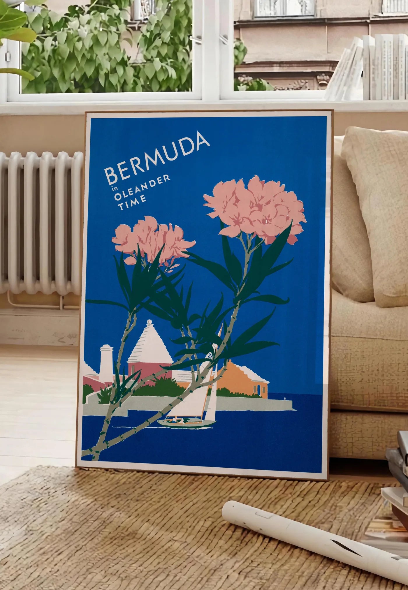 Poster affiche Bermudes vintage, posee au sol dans un salon parisien, devant une grande fenetre donnant sur un immeuble haussmannien, entre un ficus et un canape creme