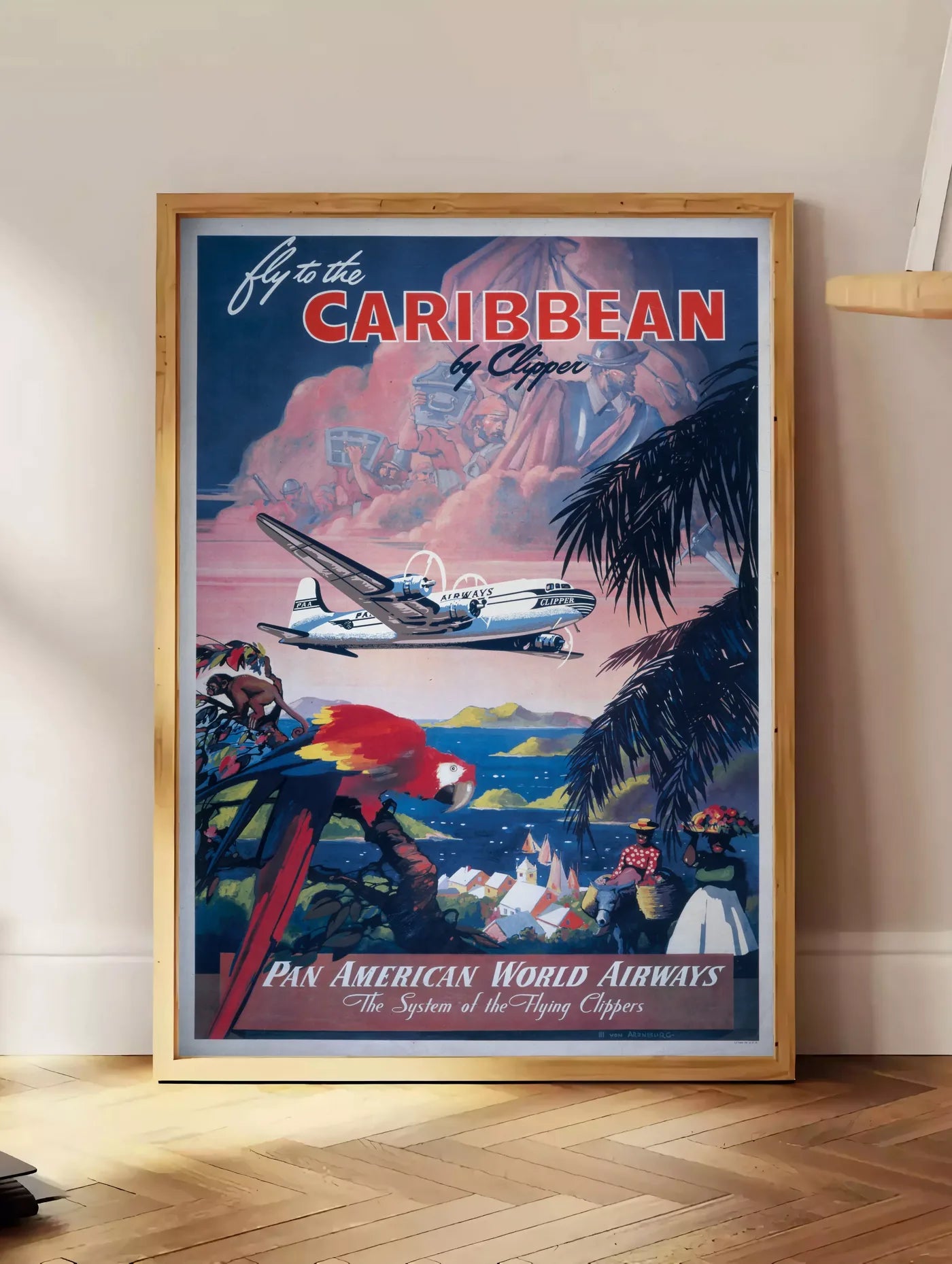 Estampe affiche Caraibes vintage, posee au sol dans un coin salon, sur un parquet a chevrons, pres d'une table d'appoint en chene chargee de livres