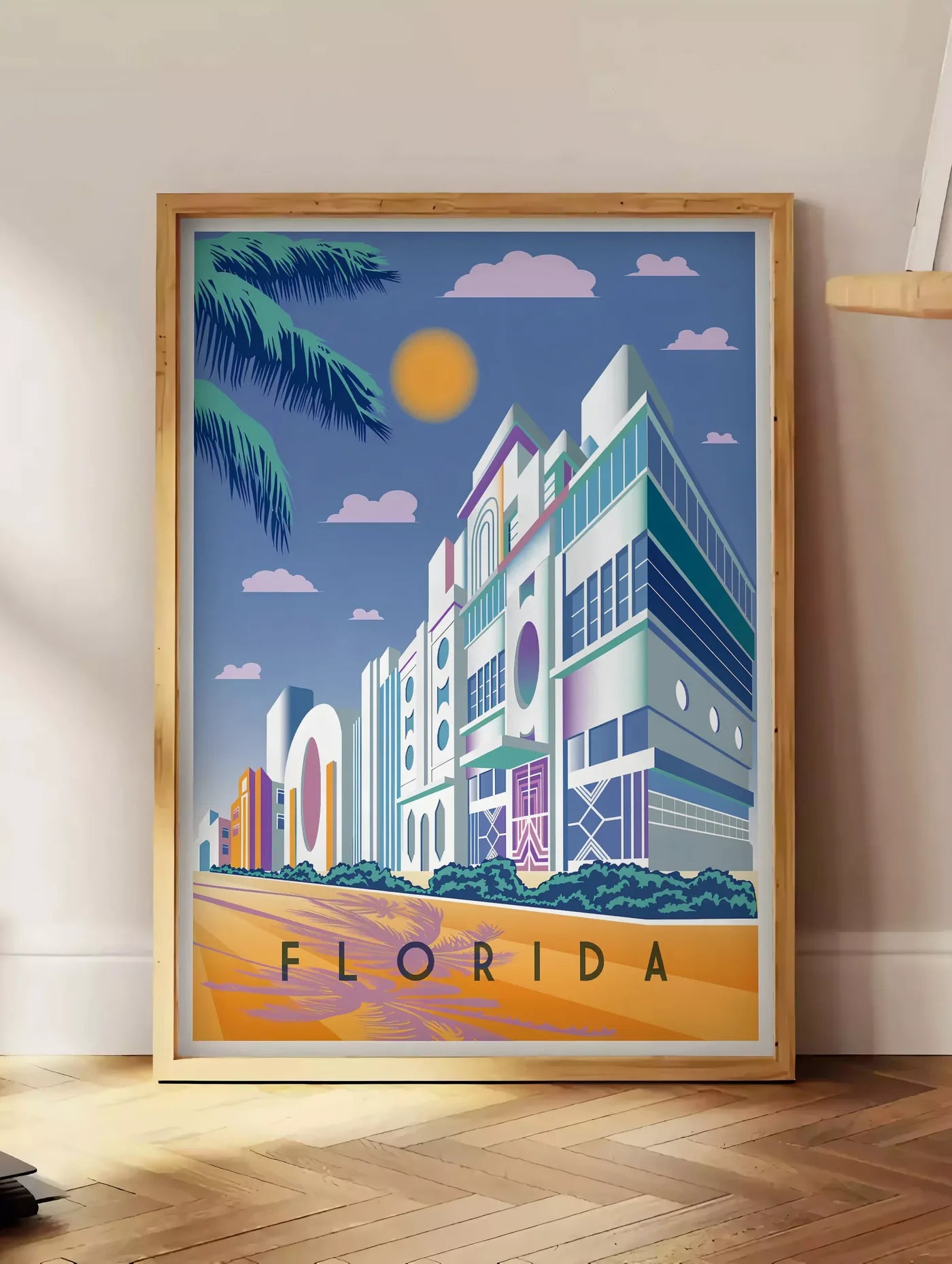 Estampe affiche Floride Art Deco, posee au sol dans un coin salon, sur un parquet a chevrons, pres d'une table d'appoint en chene chargee de livres