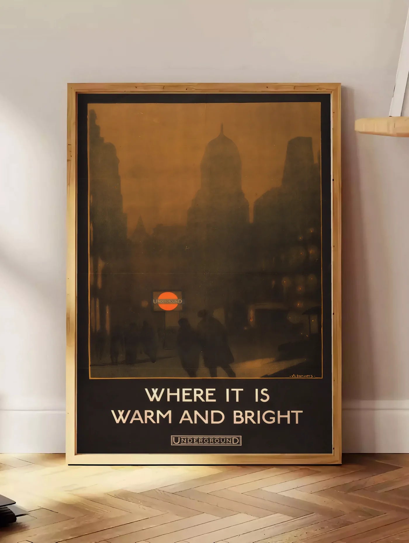 Estampe affiche Londres vintage, posee au sol dans un coin salon, sur un parquet a chevrons, pres d'une table d'appoint en chene chargee de livres