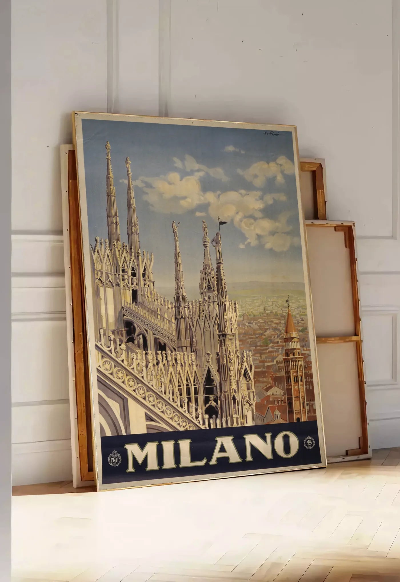 Tirage encadrable affiche Milano vintage, posee au sol dans une entree lumineuse, contre un mur a panneaux blancs, a cote de chassis en bois empiles