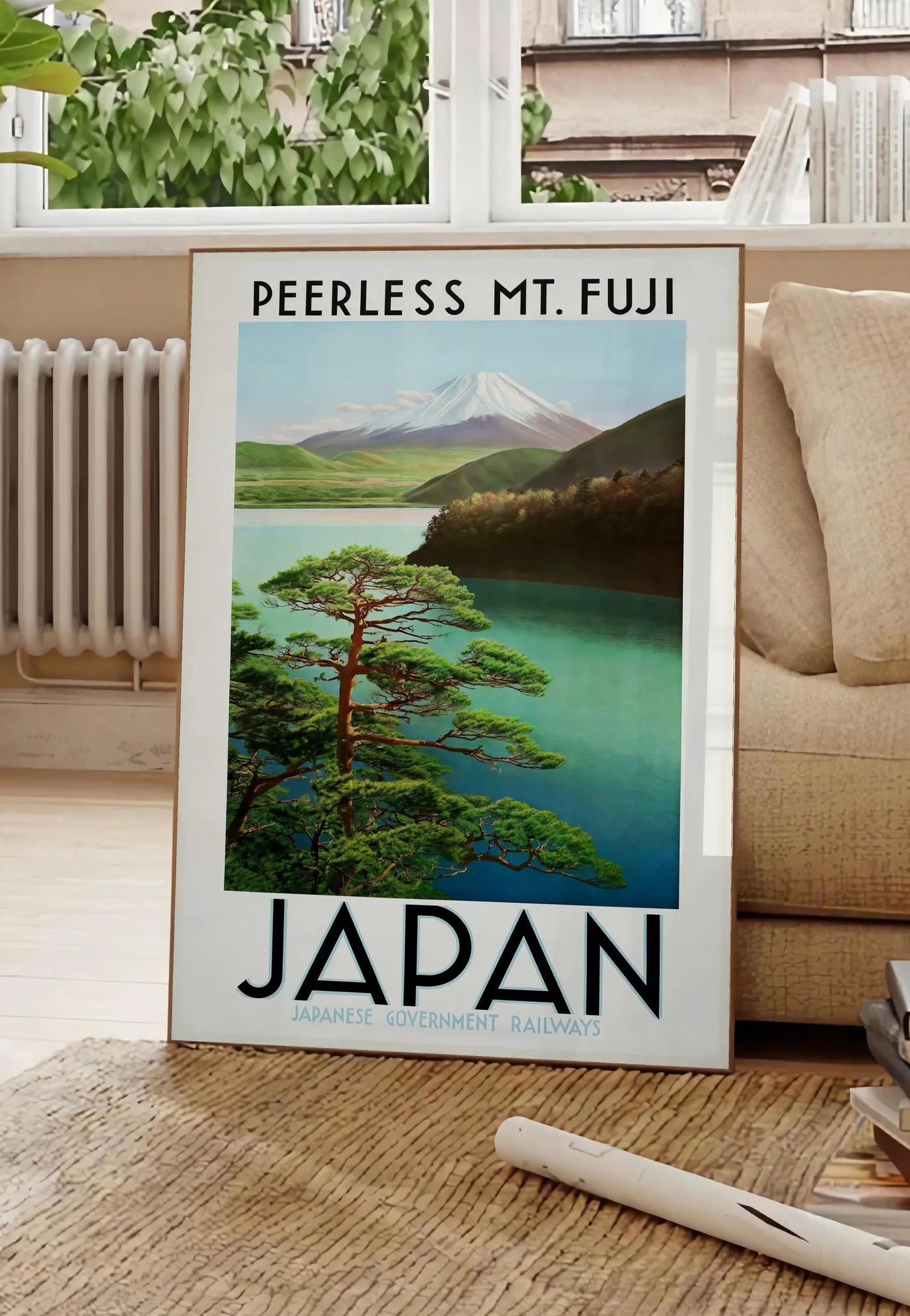 Poster affiche mont Fuji voyage vintage art japonais, posee au sol dans un salon parisien, devant une grande fenetre donnant sur un immeuble haussmannien, entre un ficus et un canape creme