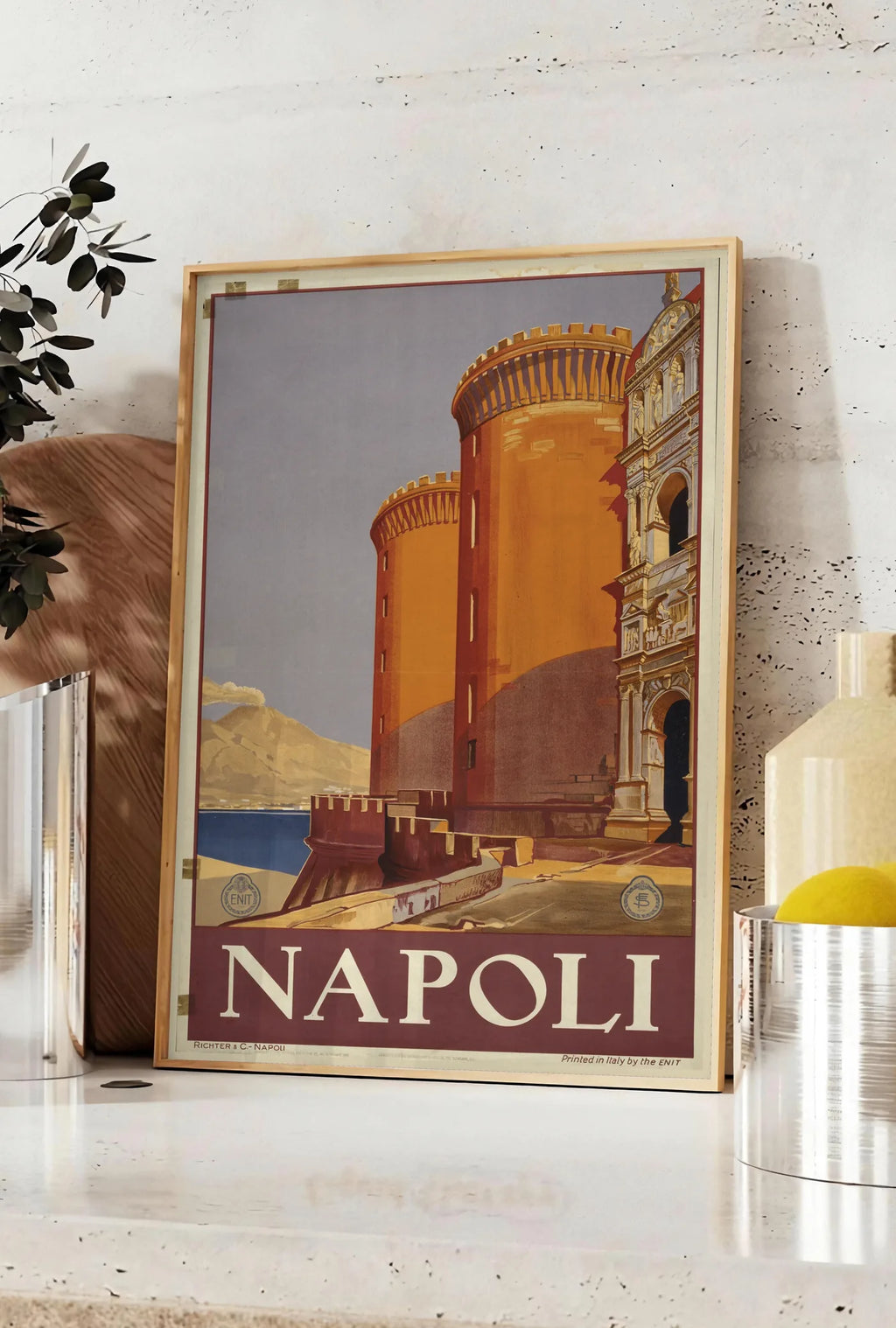 Affiche affiche Napoli vintage ENIT, posee sur un plan de travail de cuisine en pierre claire, entre une branche d'eucalyptus en vase et un bocal de citrons
