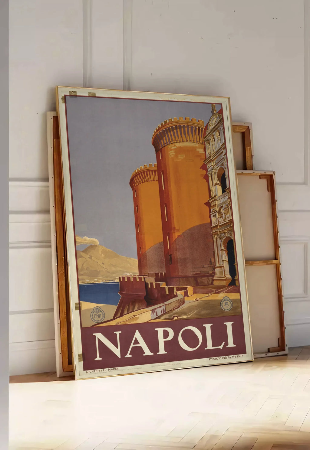Tirage encadrable affiche Napoli vintage ENIT, posee au sol dans une entree lumineuse, contre un mur a panneaux blancs, a cote de chassis en bois empiles