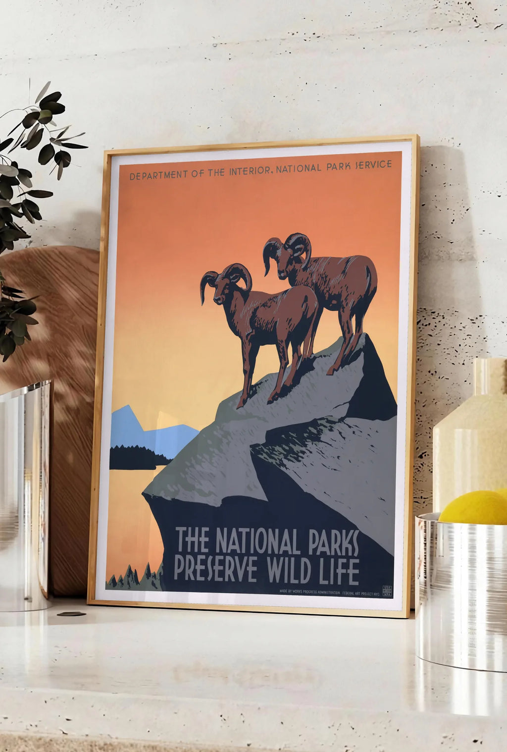 Affiche affiche mouflons National Parks vintage, posee sur un plan de travail de cuisine en pierre claire, entre une branche d'eucalyptus en vase et un bocal de citrons