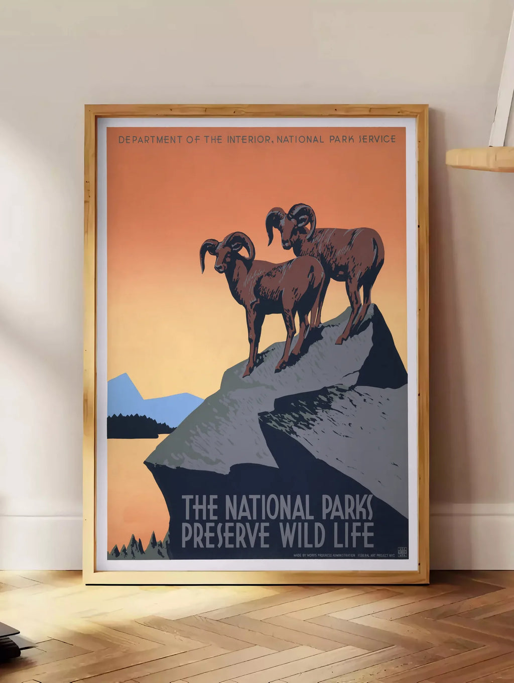 Estampe affiche mouflons National Parks vintage, posee au sol dans un coin salon, sur un parquet a chevrons, pres d'une table d'appoint en chene chargee de livres