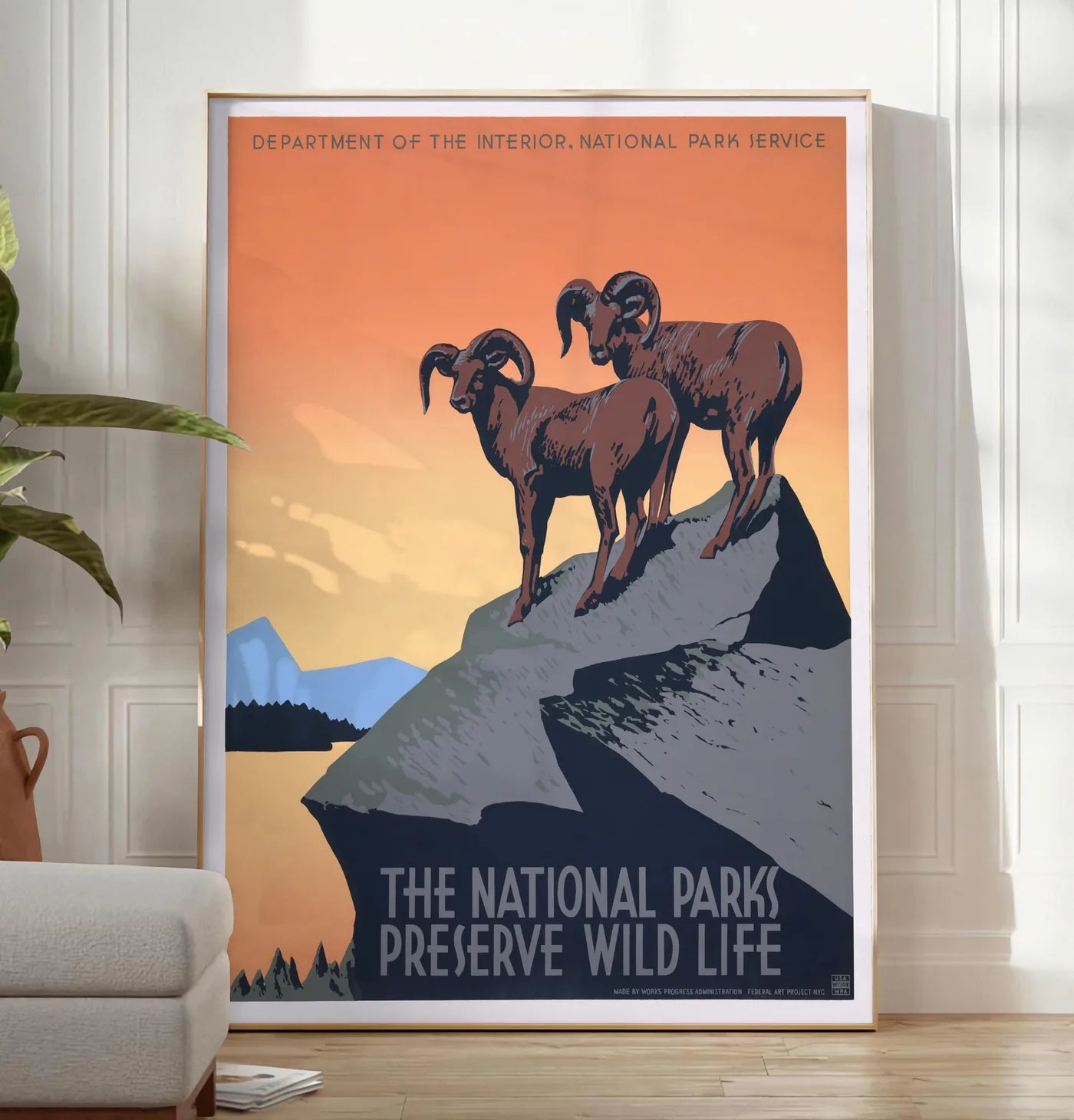 Reproduction affiche mouflons National Parks vintage, posee au sol dans un salon minimaliste clair, a cote d'un canape beige et d'une plante verte, sur un parquet clair