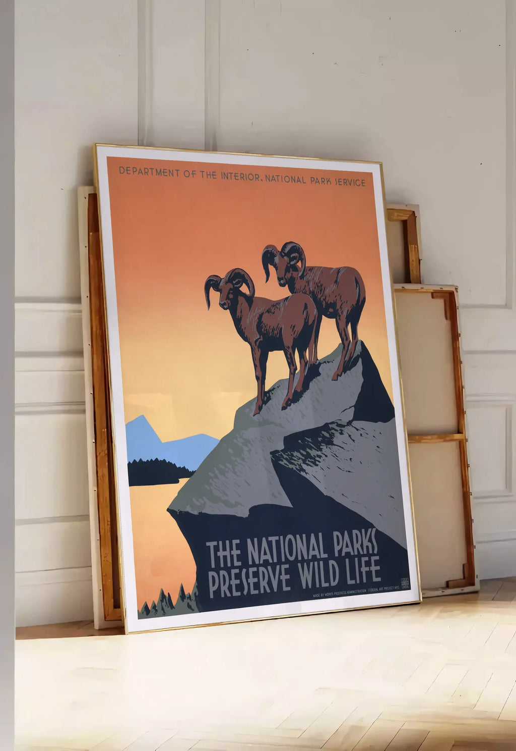 Tirage encadrable affiche mouflons National Parks vintage, posee au sol dans une entree lumineuse, contre un mur a panneaux blancs, a cote de chassis en bois empiles