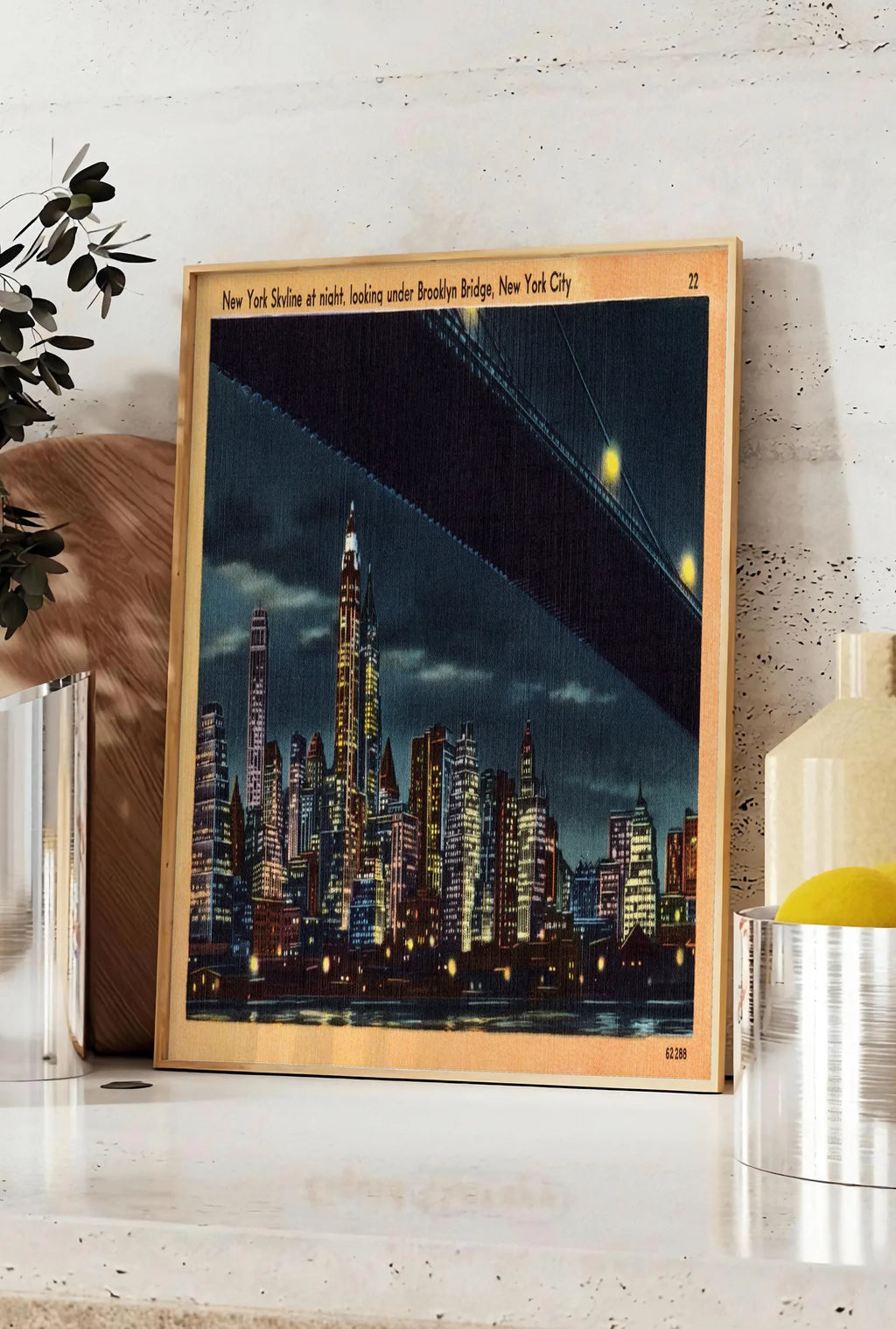 Affiche skyline de New York nocturne, posee sur un plan de travail de cuisine en pierre claire, entre une branche d'eucalyptus en vase et un bocal de citrons