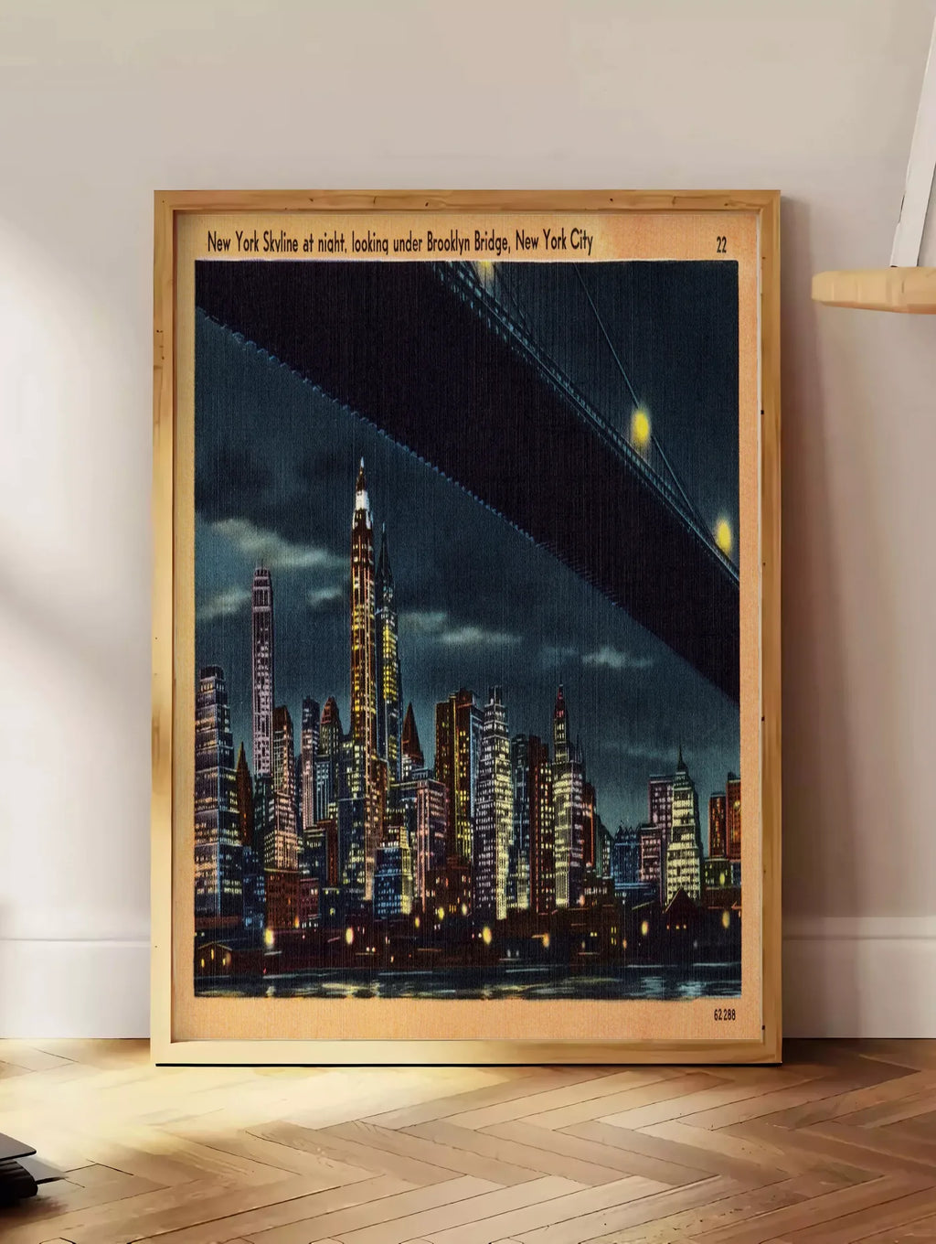 Estampe skyline de New York nocturne, posee au sol dans un coin salon, sur un parquet a chevrons, pres d'une table d'appoint en chene chargee de livres