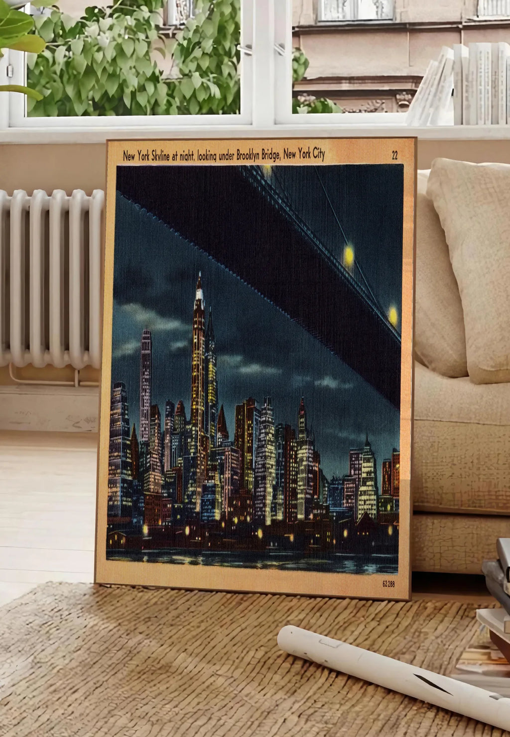 Poster skyline de New York nocturne, posee au sol dans un salon parisien, devant une grande fenetre donnant sur un immeuble haussmannien, entre un ficus et un canape creme