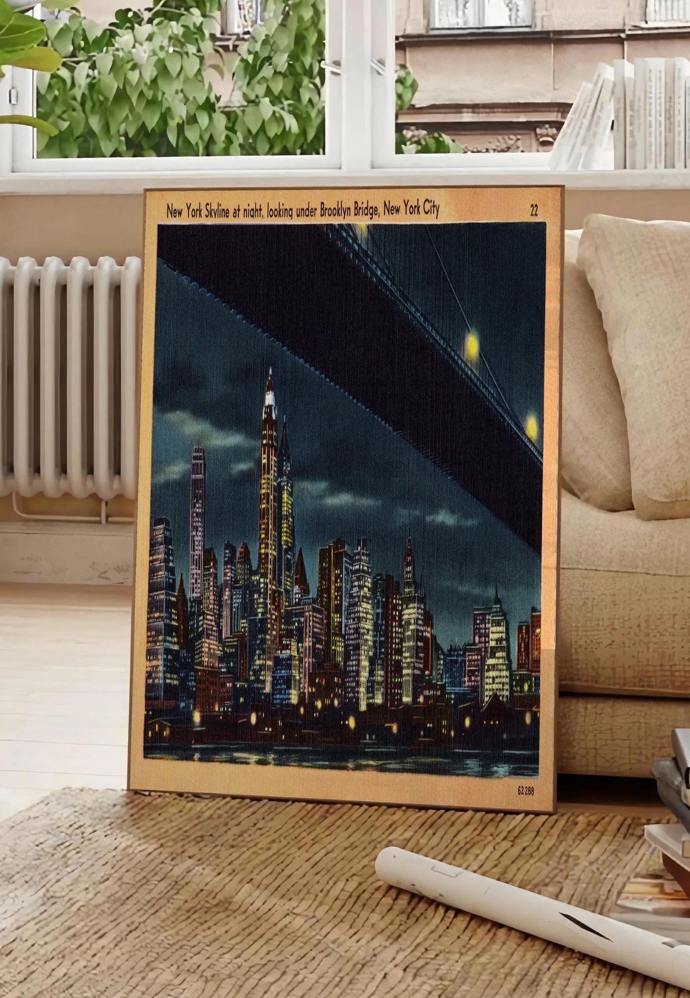 Poster skyline de New York nocturne, posee au sol dans un salon parisien, devant une grande fenetre donnant sur un immeuble haussmannien, entre un ficus et un canape creme