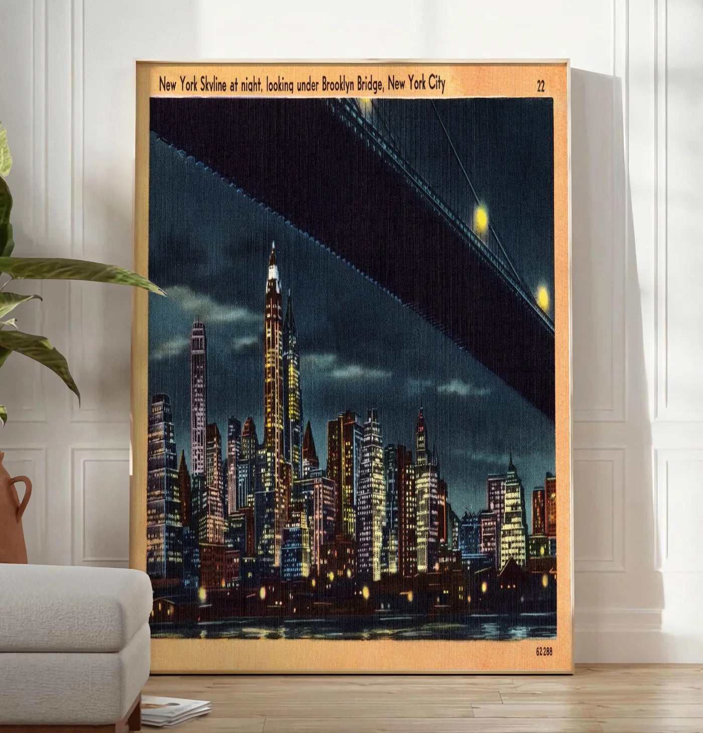 Reproduction skyline de New York nocturne, posee au sol dans un salon minimaliste clair, a cote d'un canape beige et d'une plante verte, sur un parquet clair