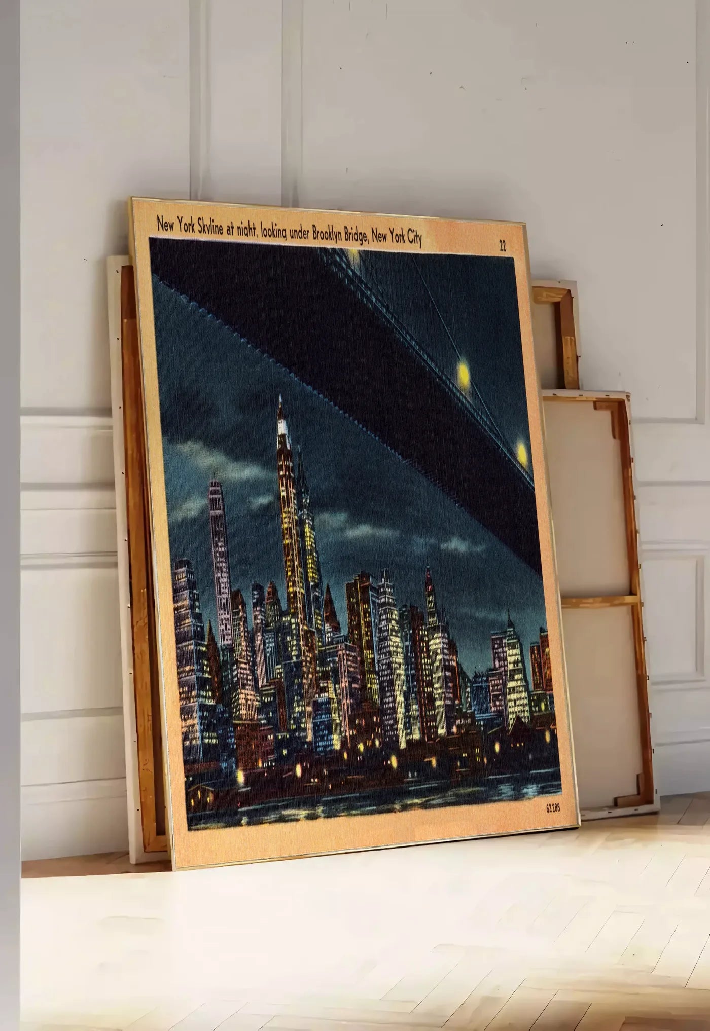 Tirage encadrable skyline de New York nocturne, posee au sol dans une entree lumineuse, contre un mur a panneaux blancs, a cote de chassis en bois empiles