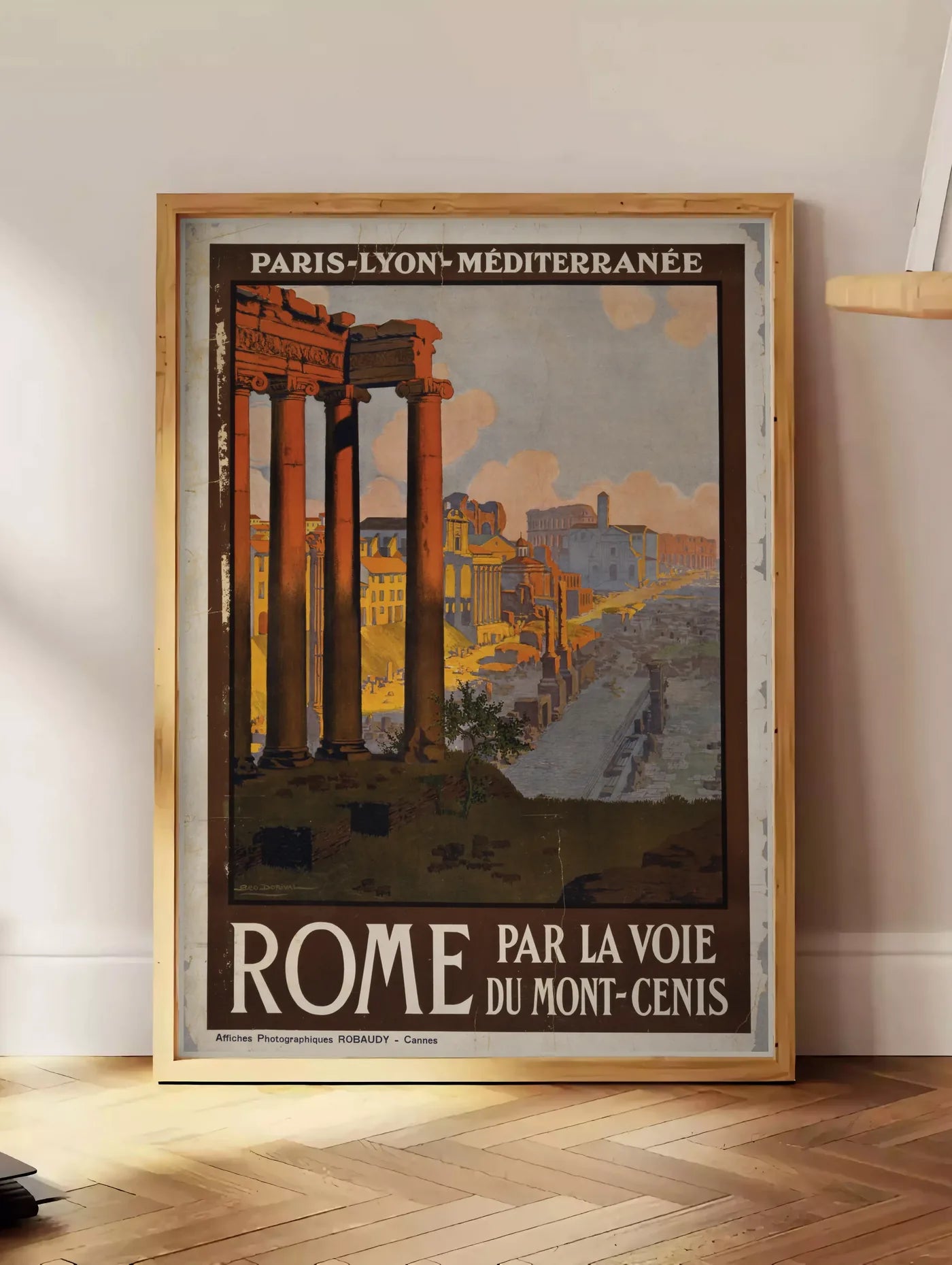 Estampe affiche Rome vintage, posee au sol dans un coin salon, sur un parquet a chevrons, pres d'une table d'appoint en chene chargee de livres