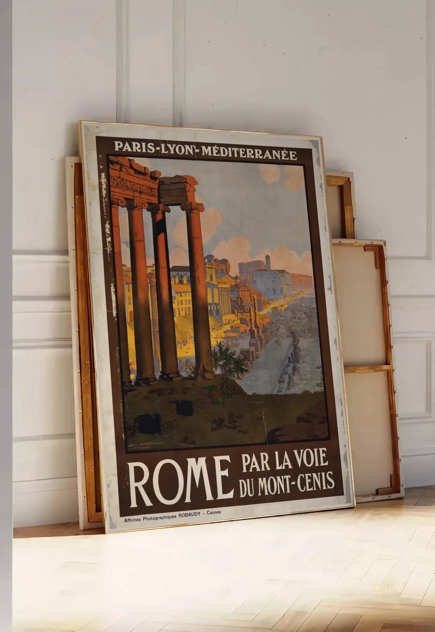 Tirage encadrable affiche Rome vintage, posee au sol dans une entree lumineuse, contre un mur a panneaux blancs, a cote de chassis en bois empiles