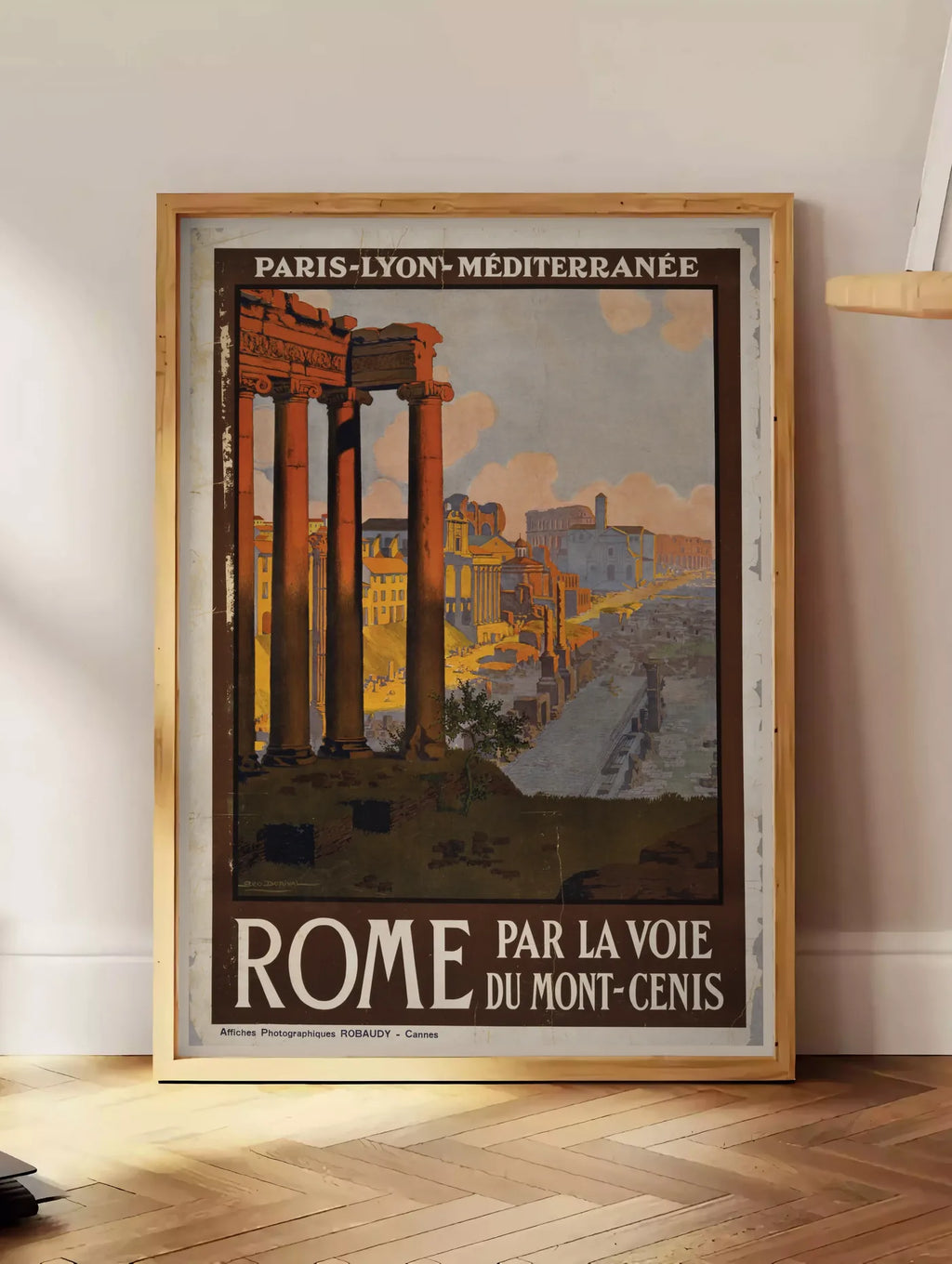 Estampe affiche Rome vintage PLM, posee au sol dans un coin salon, sur un parquet a chevrons, pres d'une table d'appoint en chene chargee de livres