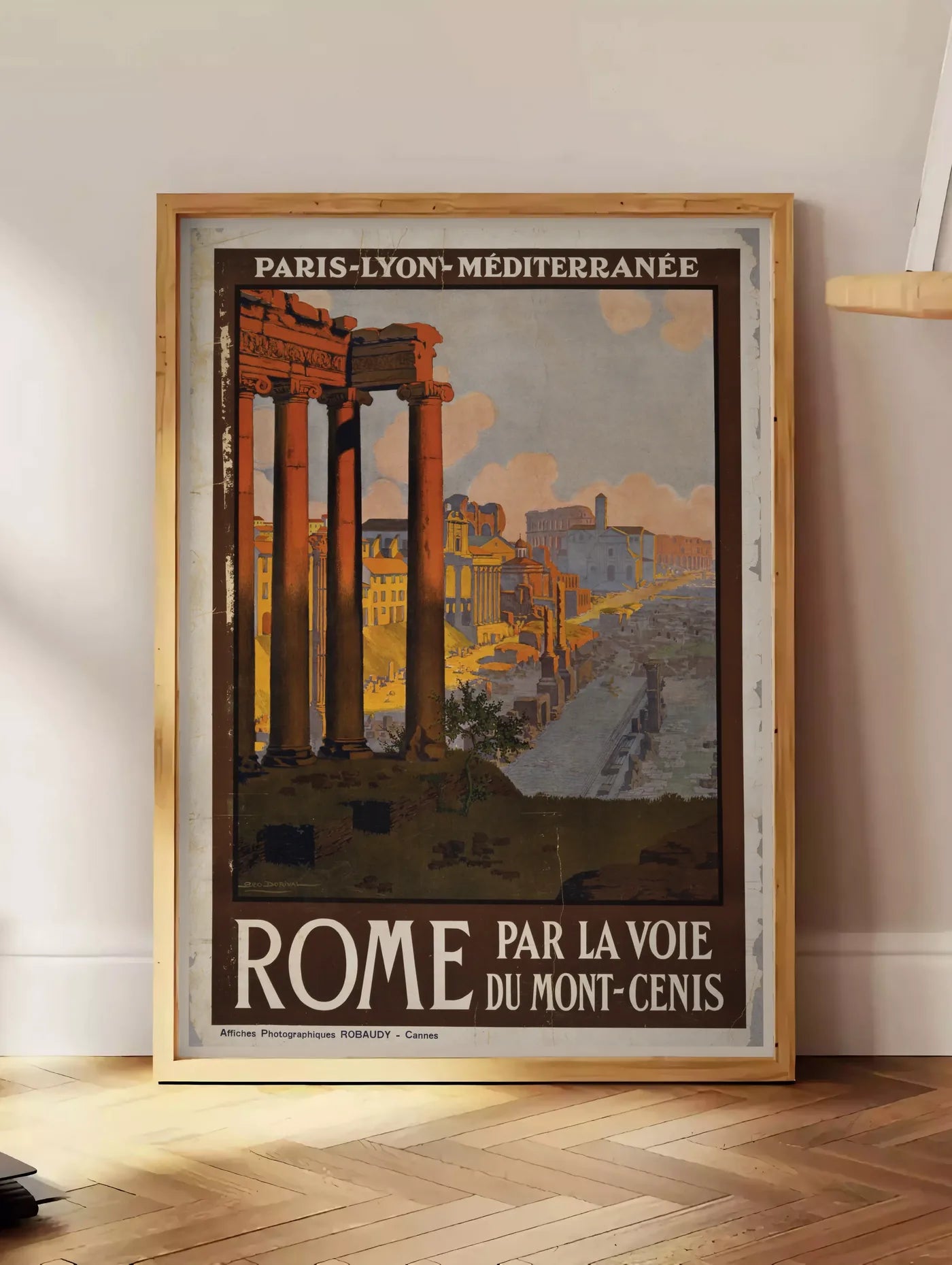 Estampe affiche Rome vintage PLM, posee au sol dans un coin salon, sur un parquet a chevrons, pres d'une table d'appoint en chene chargee de livres