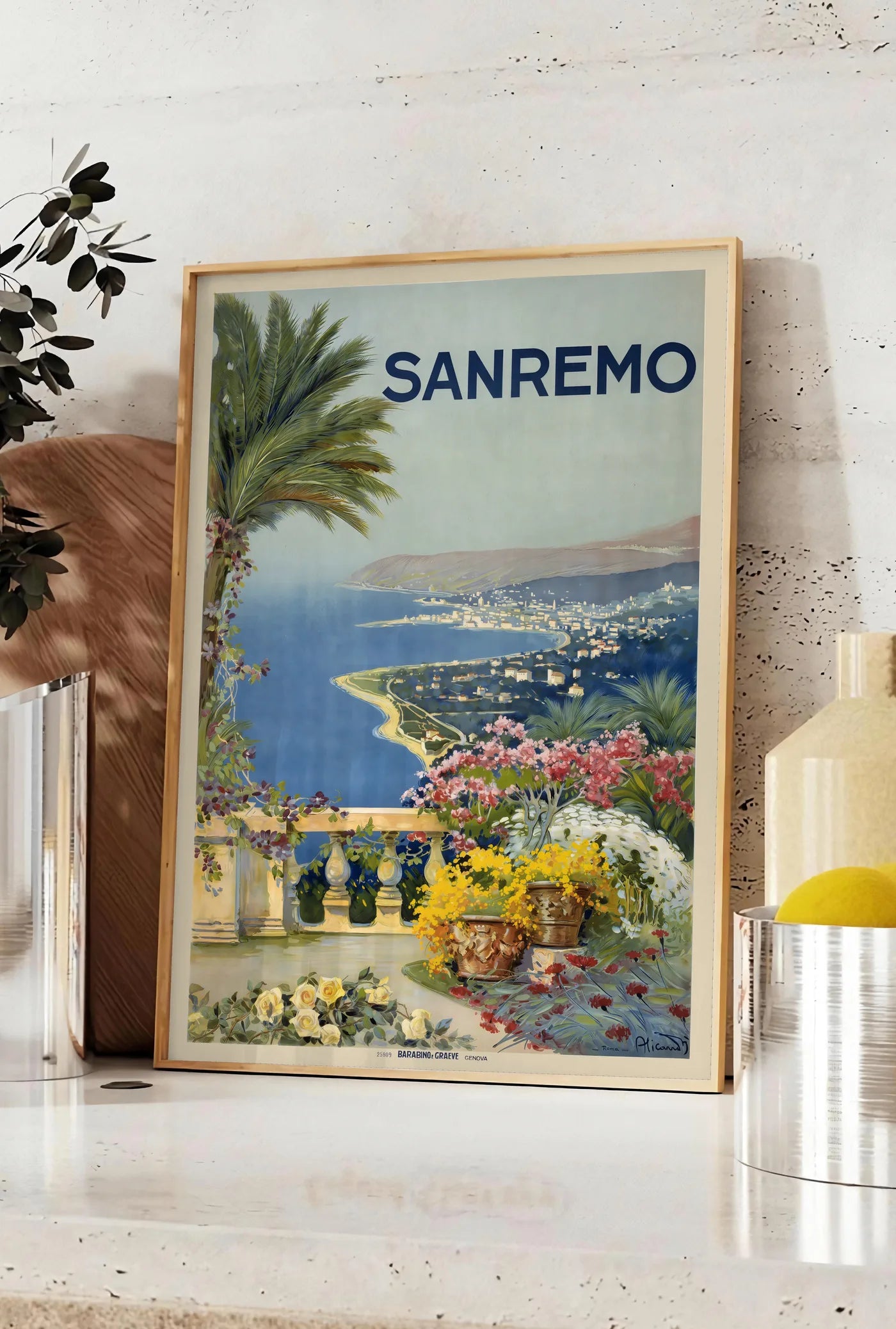 Affiche affiche Sanremo vintage, posee sur un plan de travail de cuisine en pierre claire, entre une branche d'eucalyptus en vase et un bocal de citrons