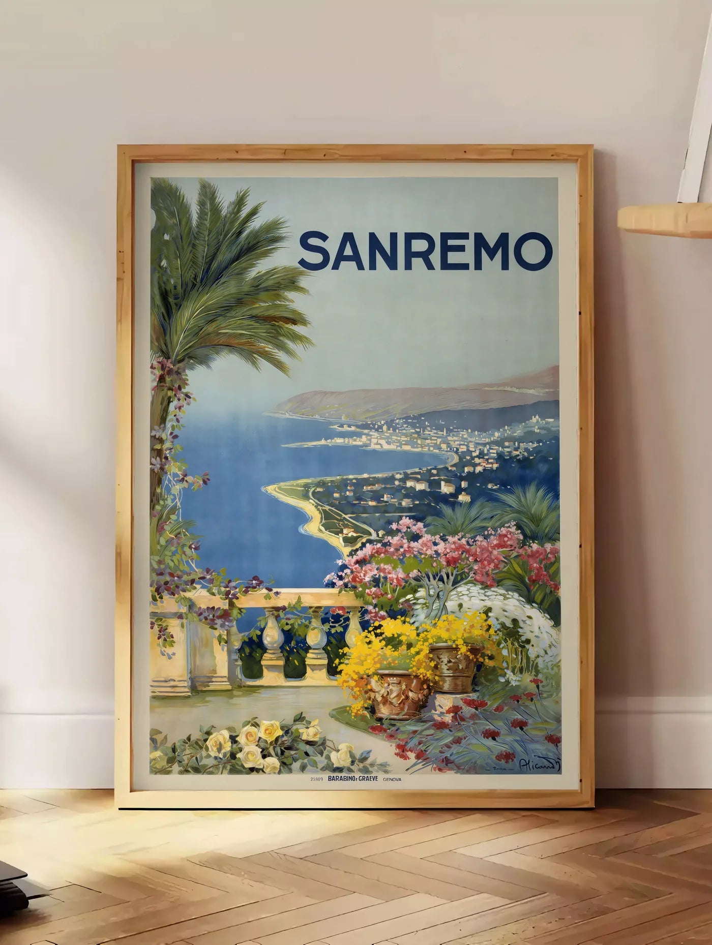 Estampe affiche Sanremo vintage, posee au sol dans un coin salon, sur un parquet a chevrons, pres d'une table d'appoint en chene chargee de livres