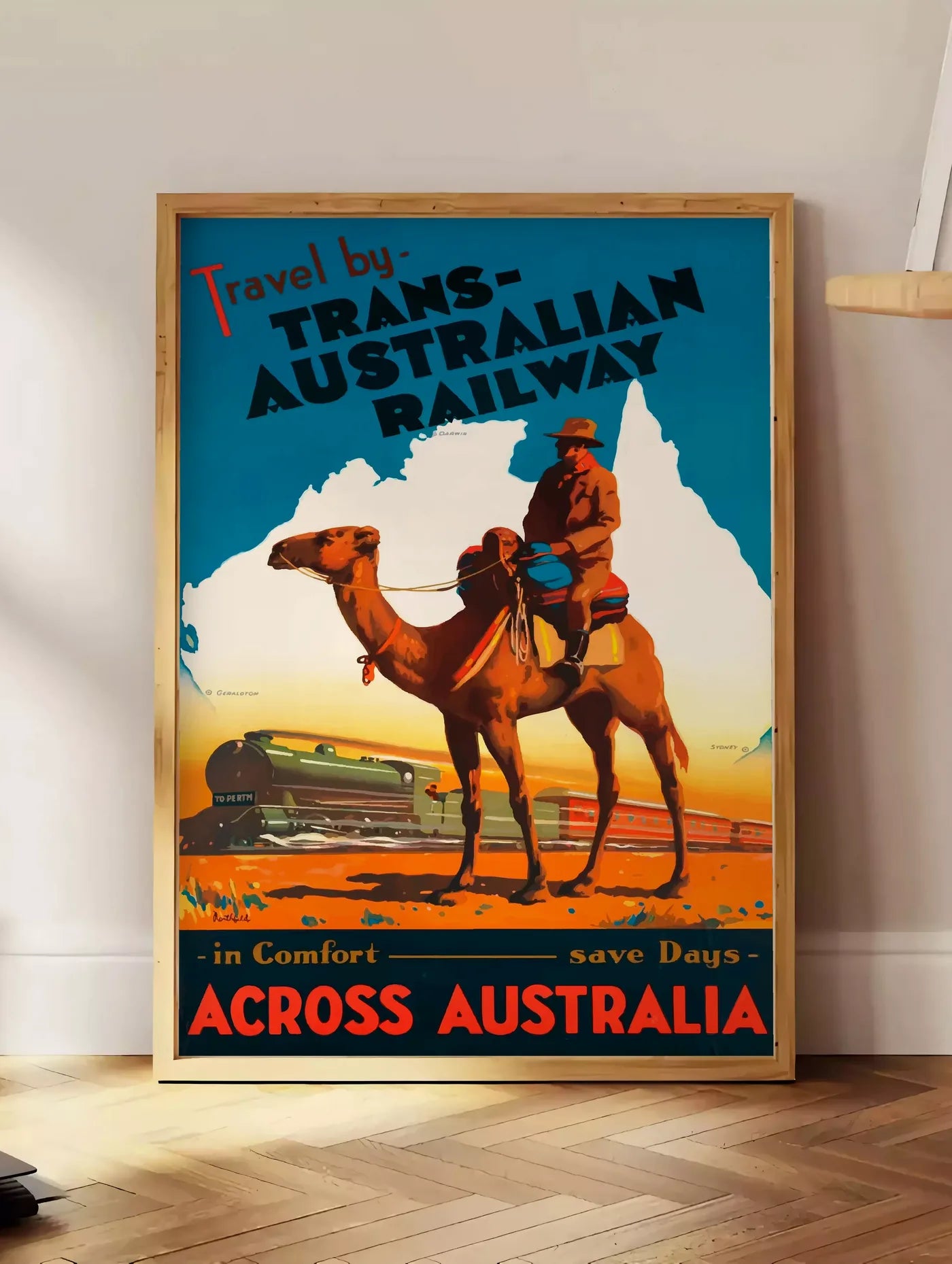 Estampe affiche Australie vintage, posee au sol dans un coin salon, sur un parquet a chevrons, pres d'une table d'appoint en chene chargee de livres