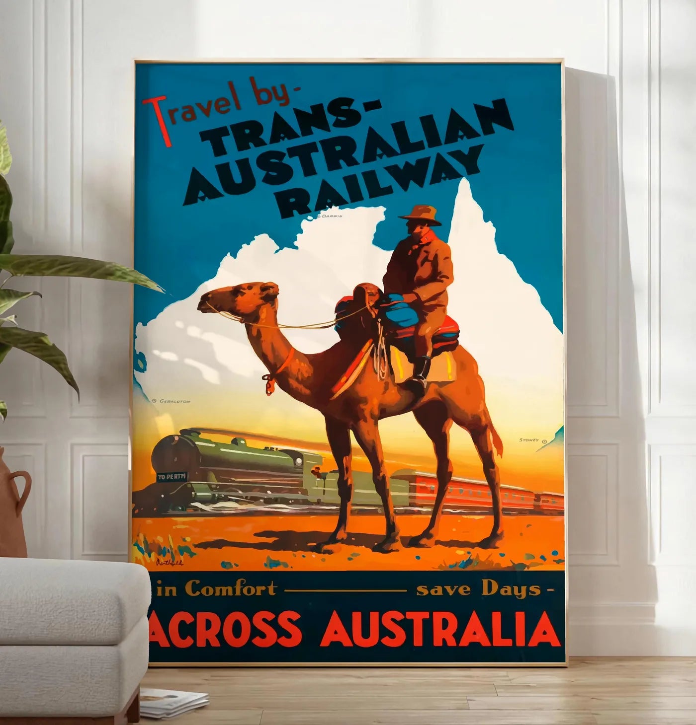Reproduction affiche Australie vintage, posee au sol dans un salon minimaliste clair, a cote d'un canape beige et d'une plante verte, sur un parquet clair