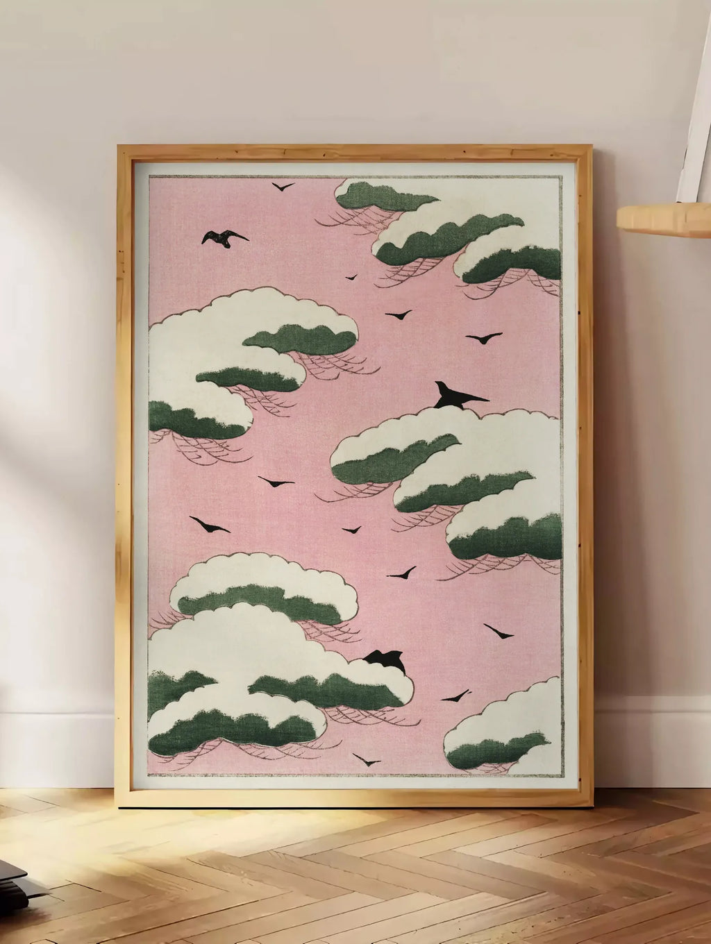Estampe affiche nuages verts et oiseaux sur ciel rose de Watanabe Seitei estampe japonaise, posee au sol dans un coin salon, sur un parquet a chevrons, pres d'une table d'appoint en chene chargee de livres