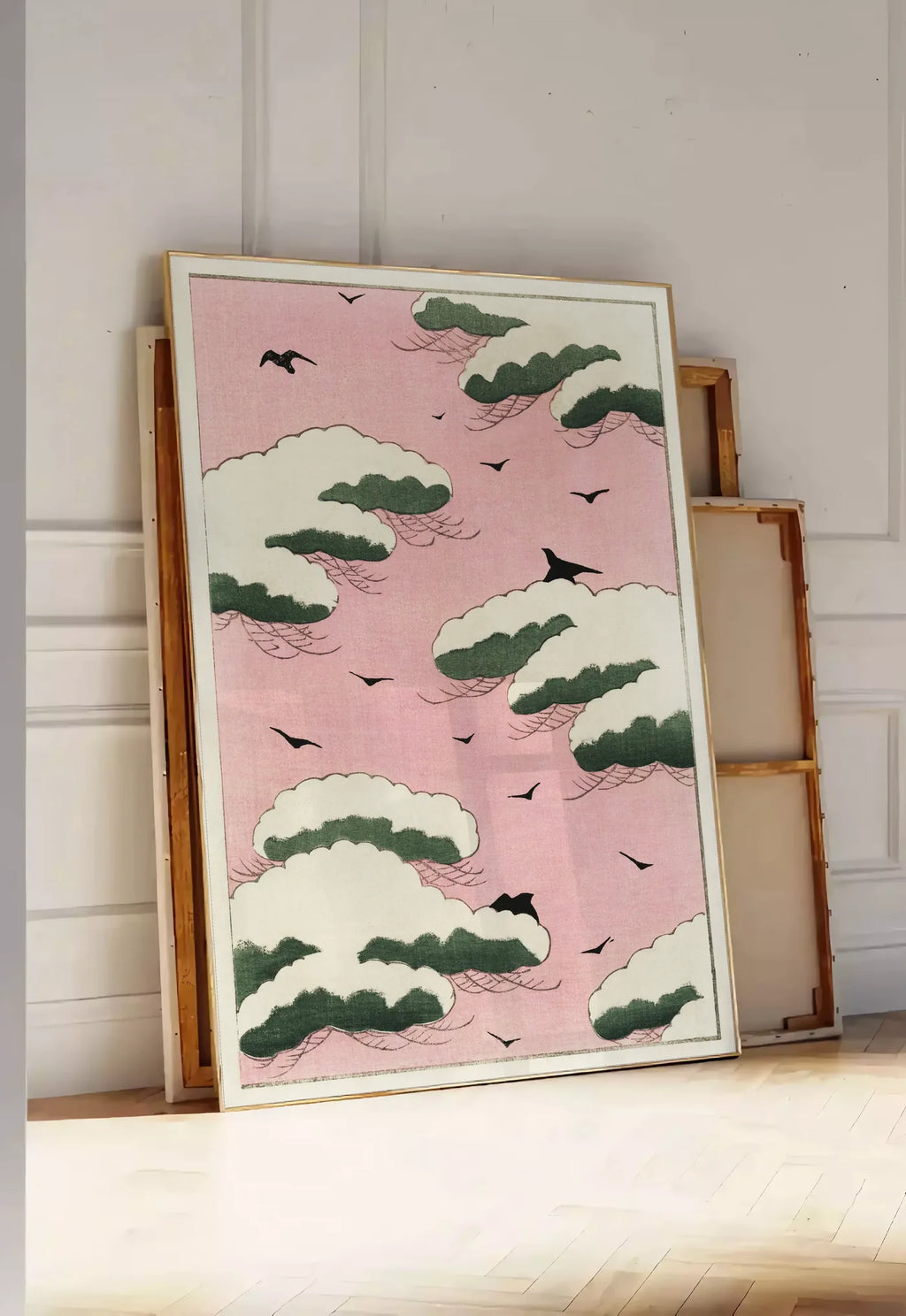 Tirage encadrable affiche nuages verts et oiseaux sur ciel rose de Watanabe Seitei estampe japonaise, posee au sol dans une entree lumineuse, contre un mur a panneaux blancs, a cote de chassis en bois empiles